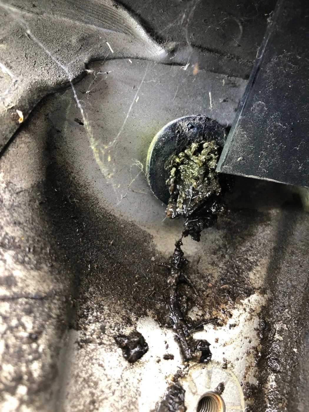 Close-up of a clogged automotive body drain opening with dirt, debris, and moisture buildup at a vehicle water-leak source.