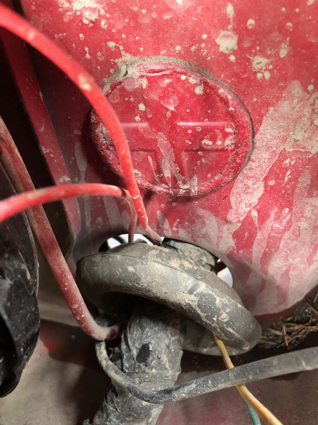 Close-up photo of dusty and dirty red machinery part with black rubber wheel and electrical wires.
