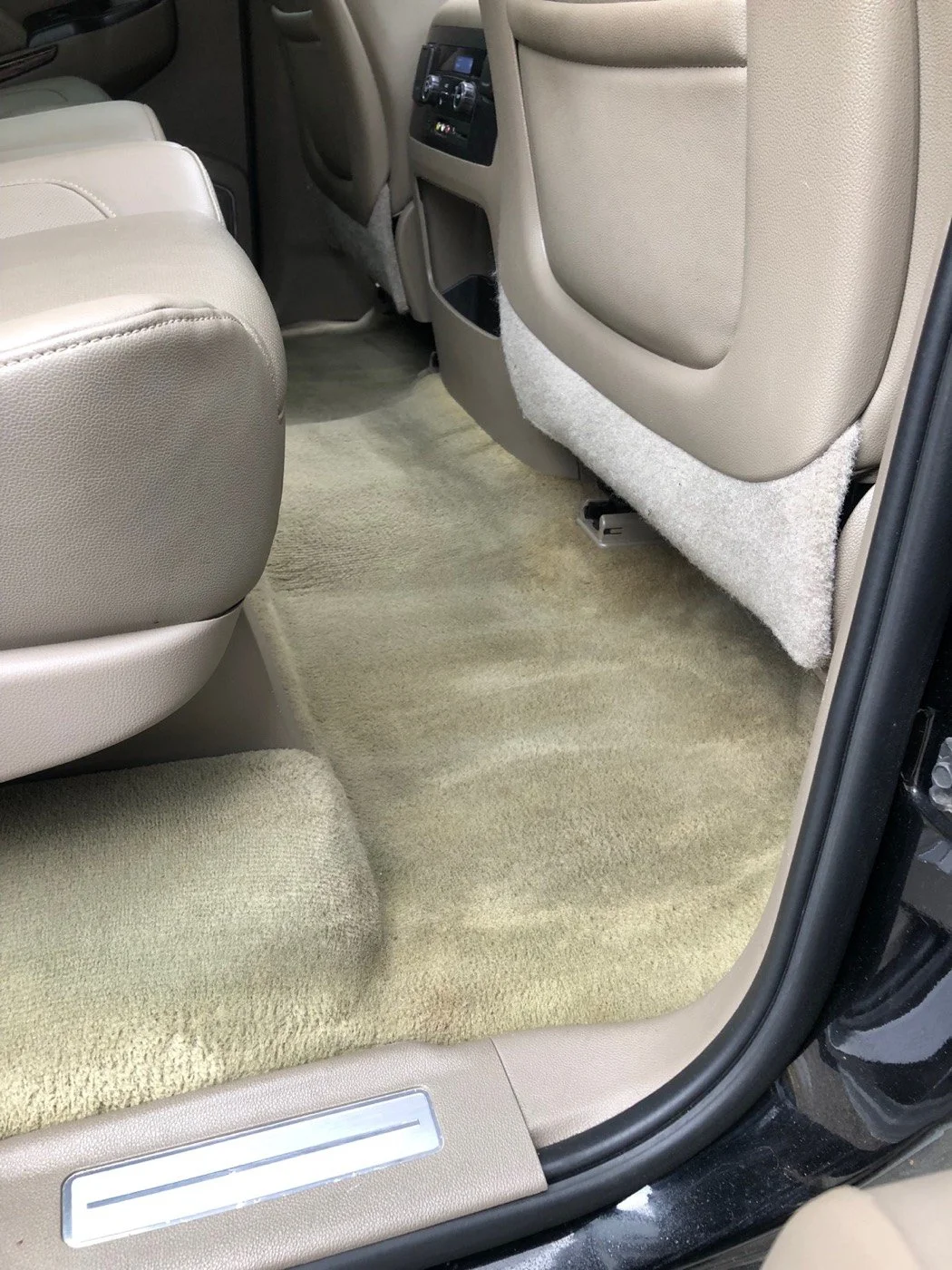 The back seat floor of a car with beige carpet and tan leather seats.