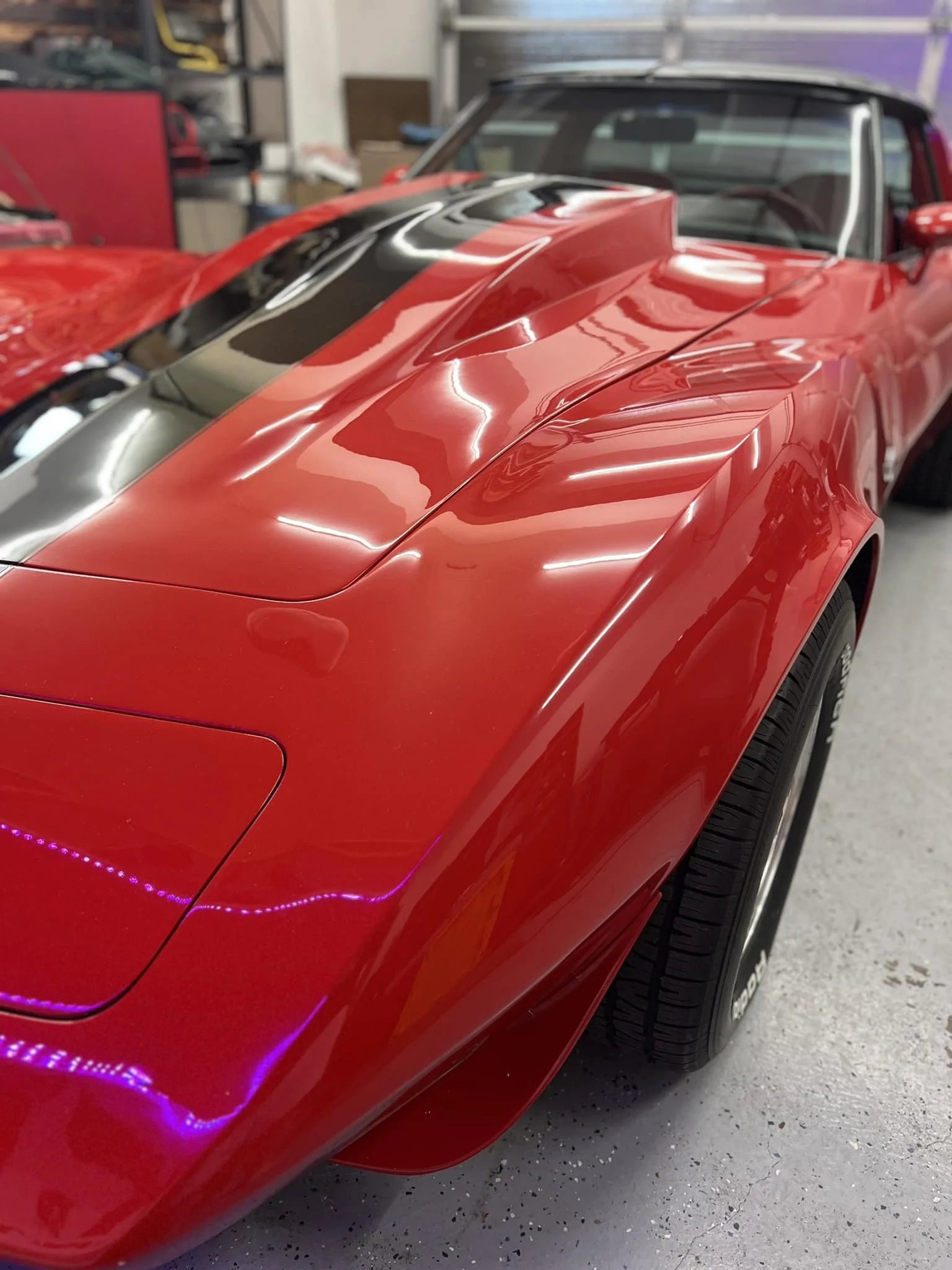 Close-up of a red sports car with a black racing stripe, parked on a garage floor.