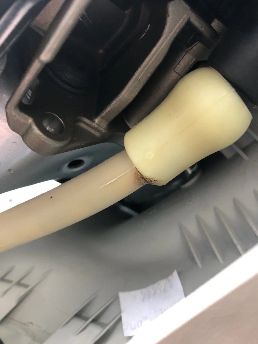 Close-up view of a mechanical component with a light-colored pipe and a black metal part, possibly part of machinery or automotive equipment, with some rust and dirt visible.