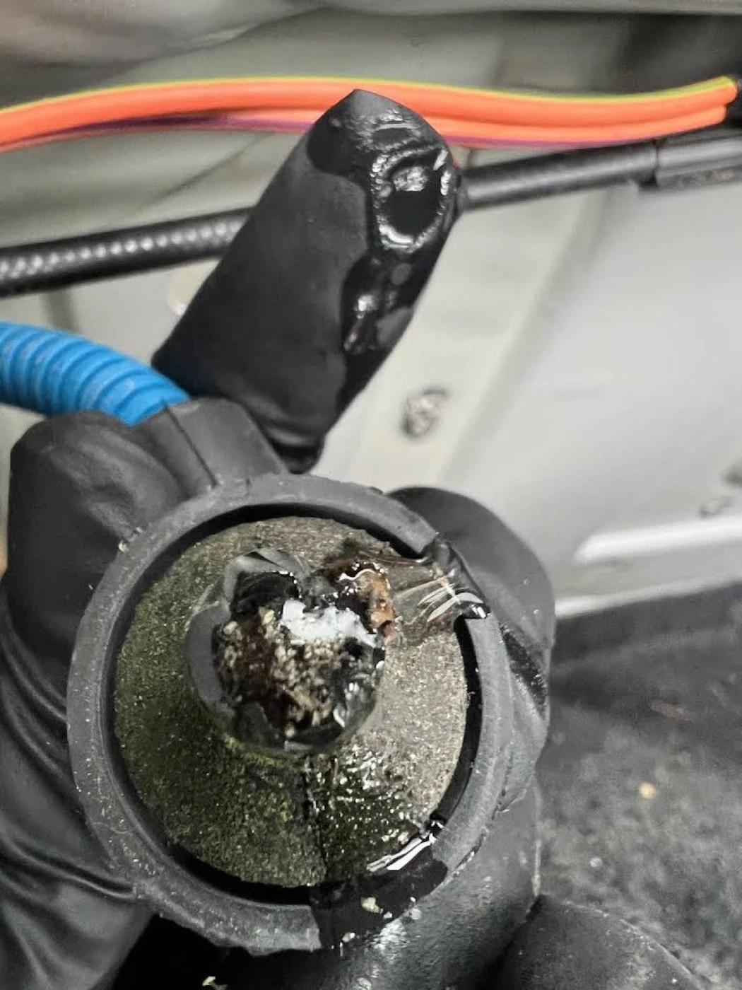 A damaged and burnt car ignition switch with melted plastic and corrosion, showing signs of electrical failure.