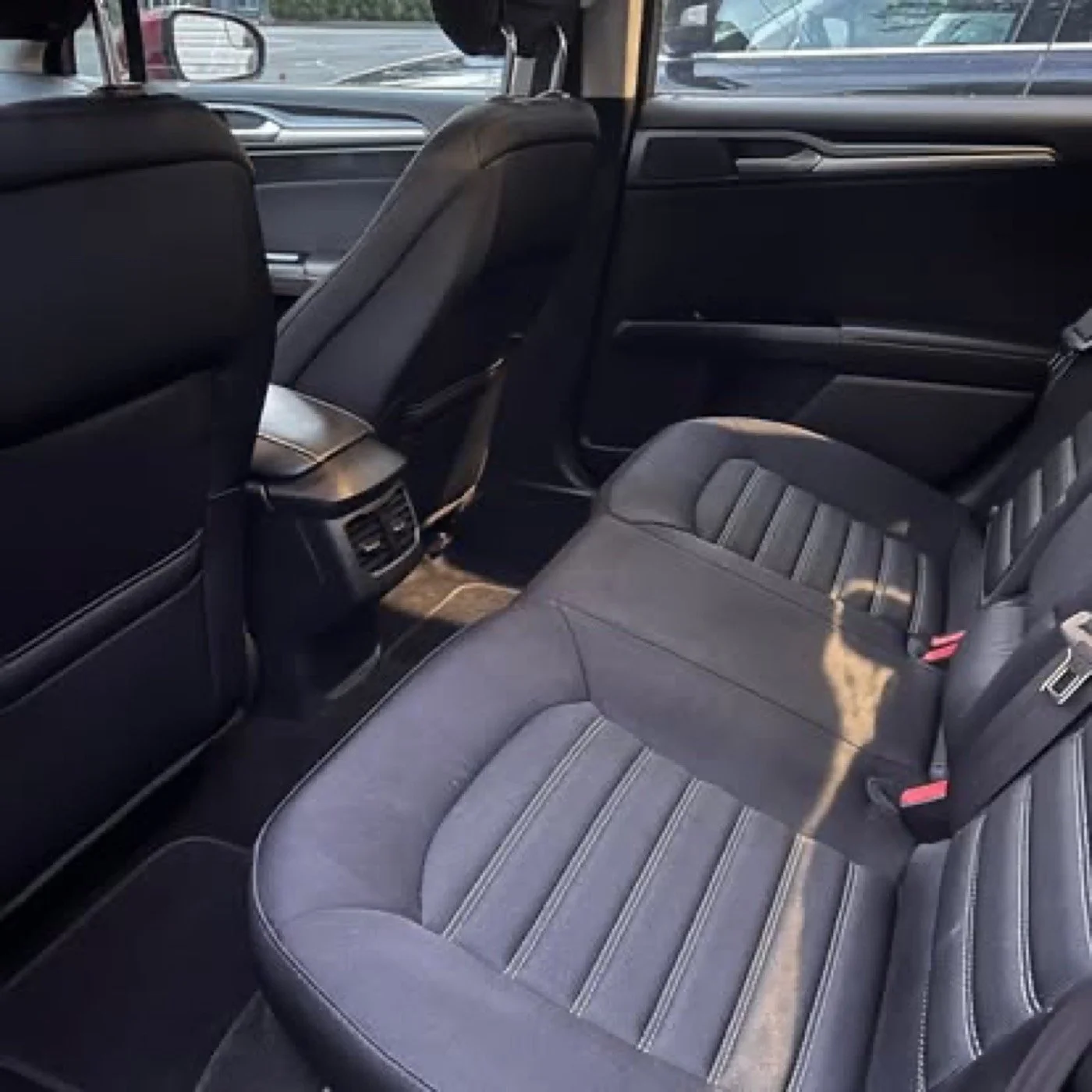Interior of a modern car showing the backseat, rear air vents, and headrests in a parking lot.