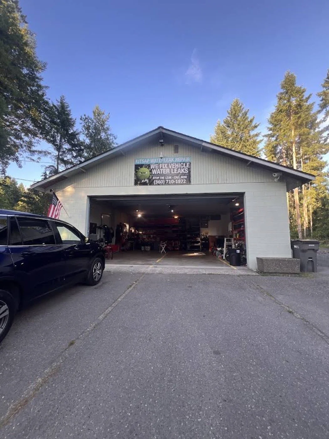 Garage with open door, cars parked outside, and a sign advertising vehicle water leak repair.