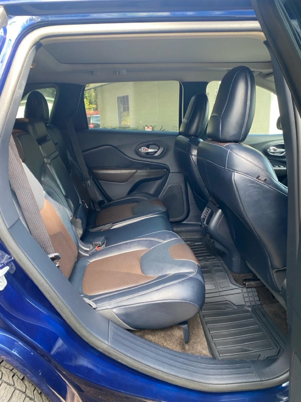 The interior of a blue SUV showing the backseat area with black and brown fabric and leather seats, a rubber floor mat, and the front seats with black leather upholstery.