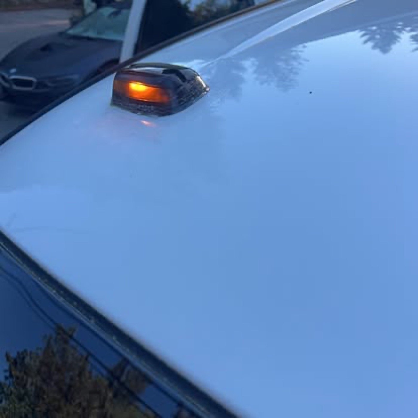 Close-up of the front of a white vehicle with a side mirror and an orange turn signal light on the fender.