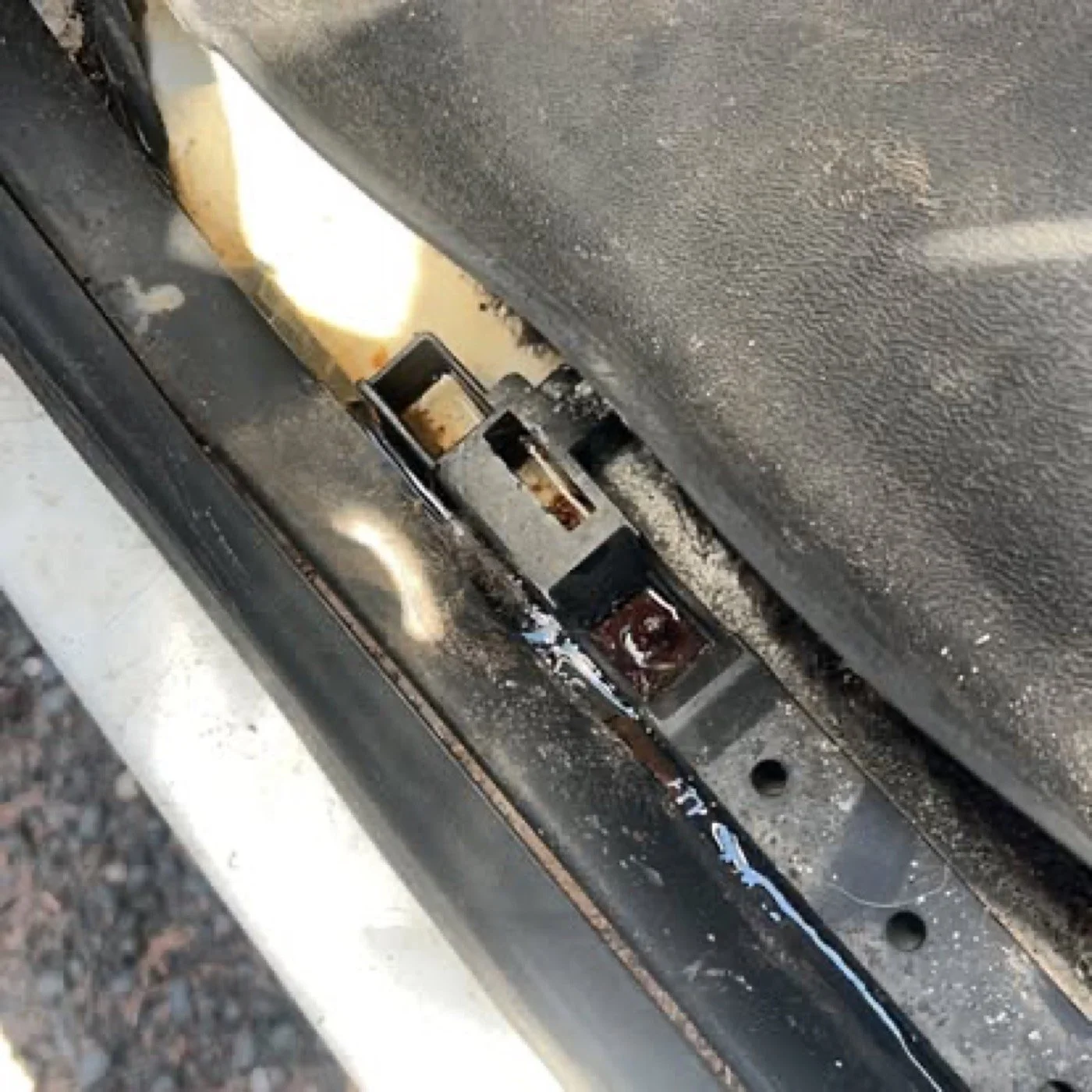 Close-up view of a dirty vehicle door latch mechanism with visible rust and grime buildup.