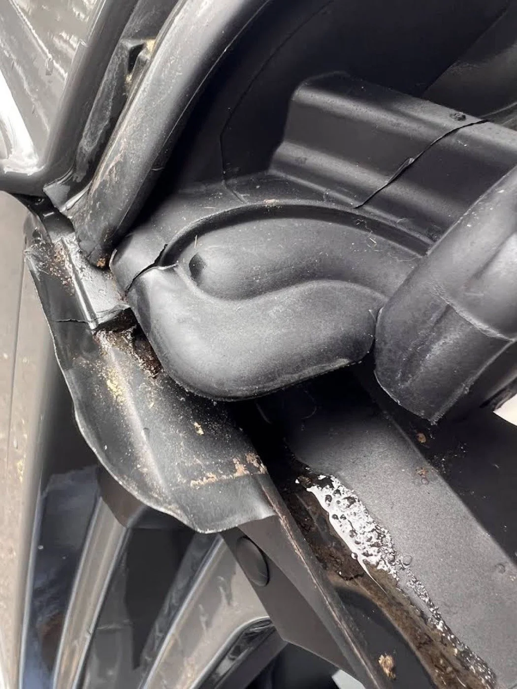 Close-up of a car wheel well showing rust and dirt buildup around the metal components.