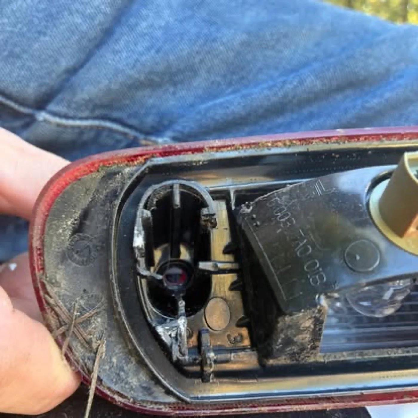 Close-up of the inside of a damaged car's headlight, showing broken and burnt internal components, with part of a person's hand holding it.