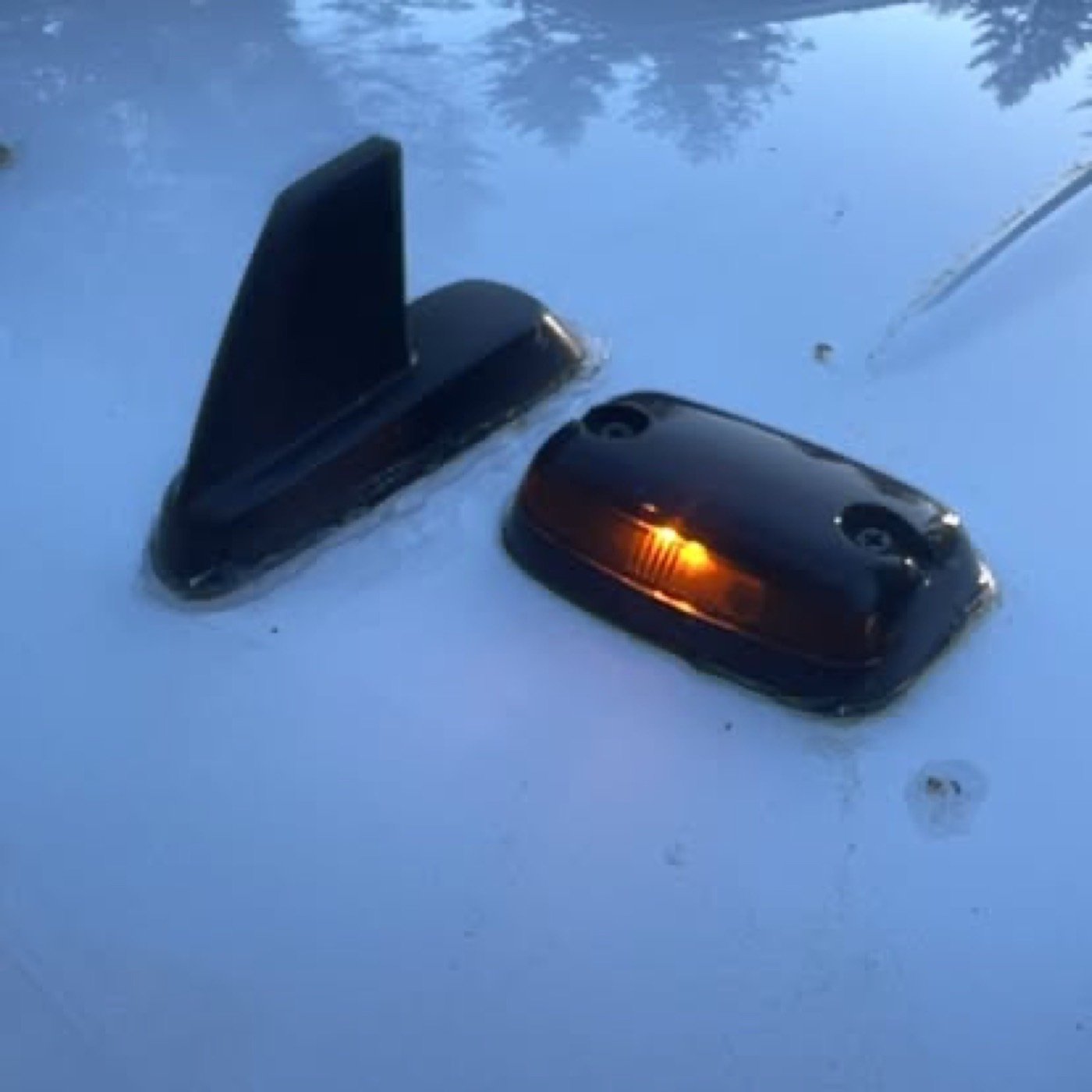 Two black car lights, one with a turning signal illuminated, are embedded in snow.