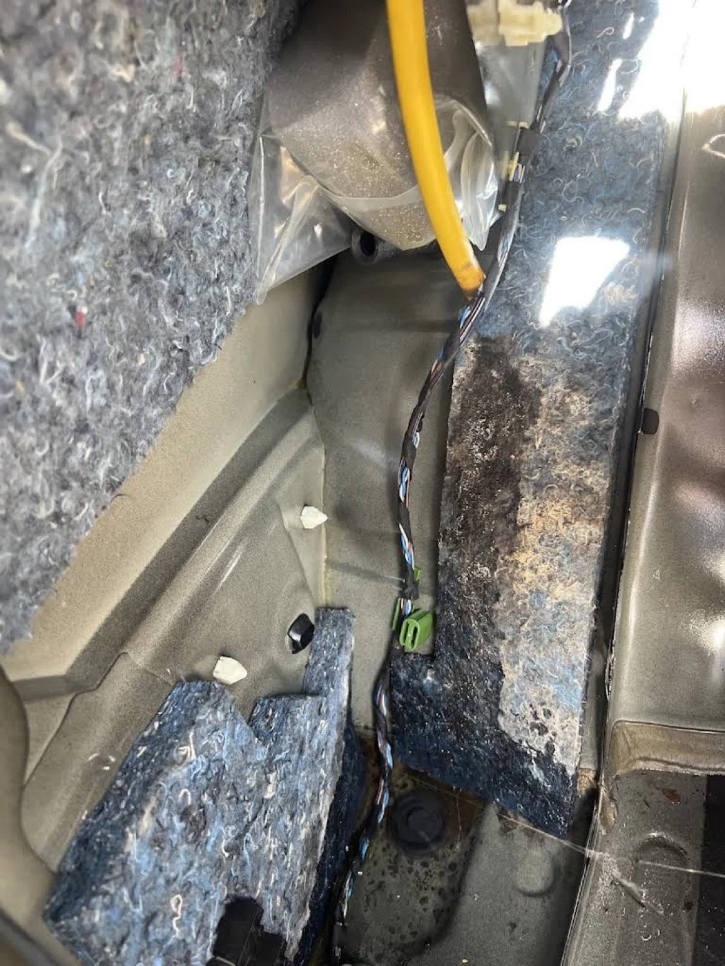 The interior of a car with the carpet removed, exposing the wiring and parts beneath the dashboard.