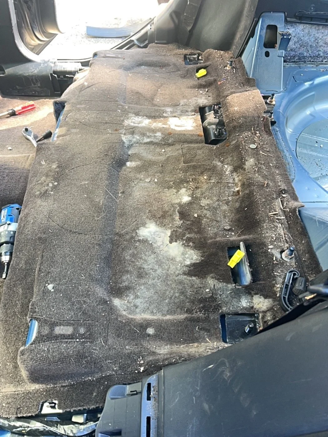 The interior of a vehicle with the seats removed, showing a dirty and worn carpeted floor with some tools around.