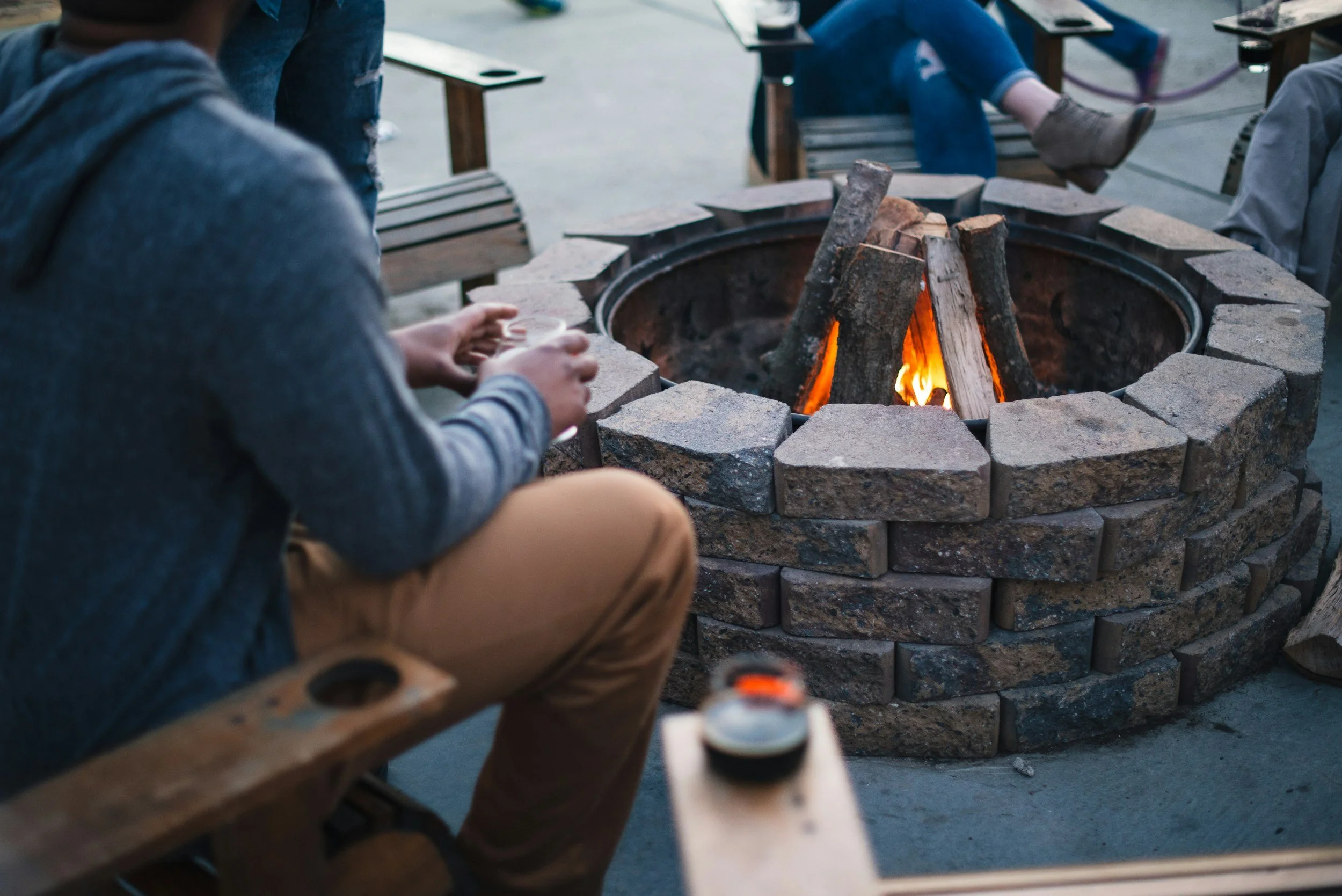People sitting around a fire pit made of bricks, cooking or preparing food outdoors.