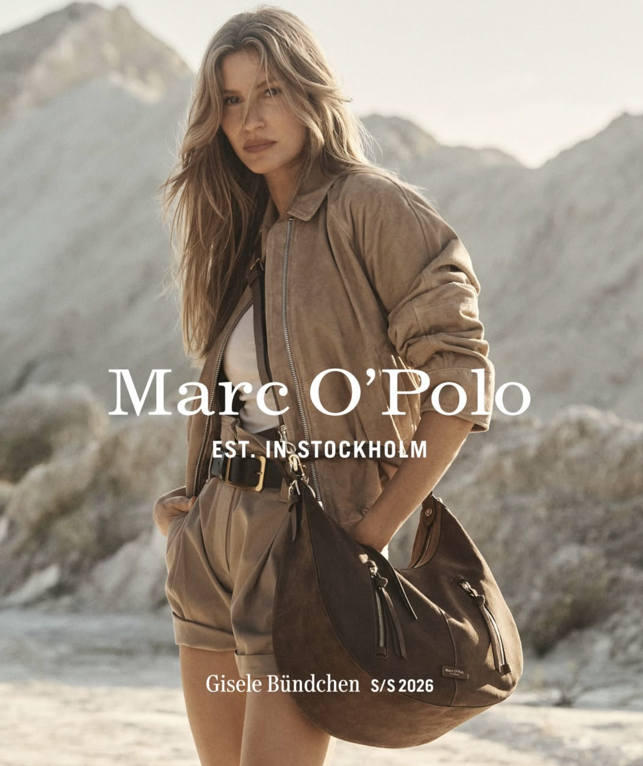 Fashion magazine cover featuring a woman in a tan jacket and shorts, standing outdoors with rocky mountains in the background, advertising Marc O'Polo for spring/summer 2026.
