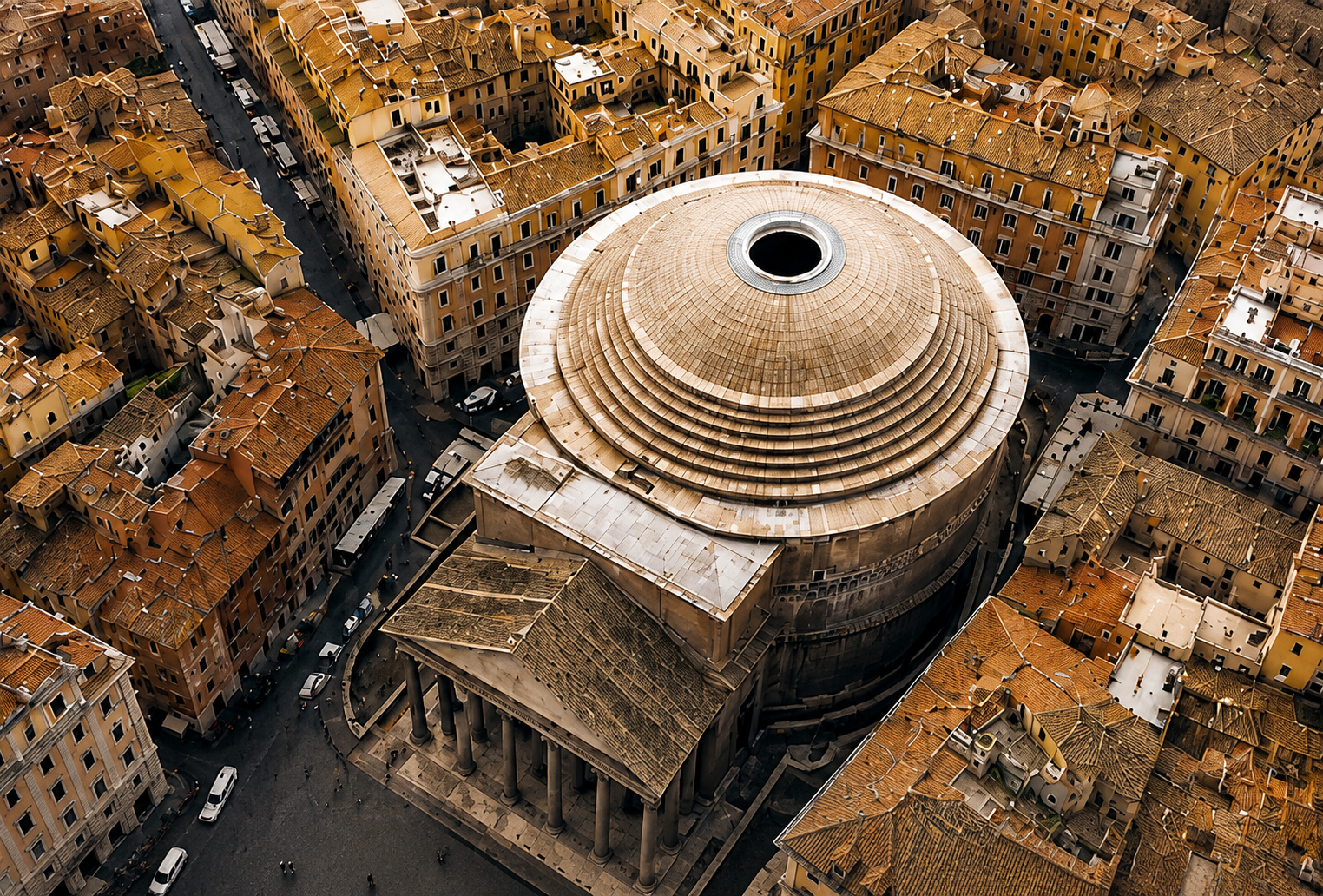 Aerial view of a round building with a large open top, surrounded by orange-tiled roof buildings on a city street.