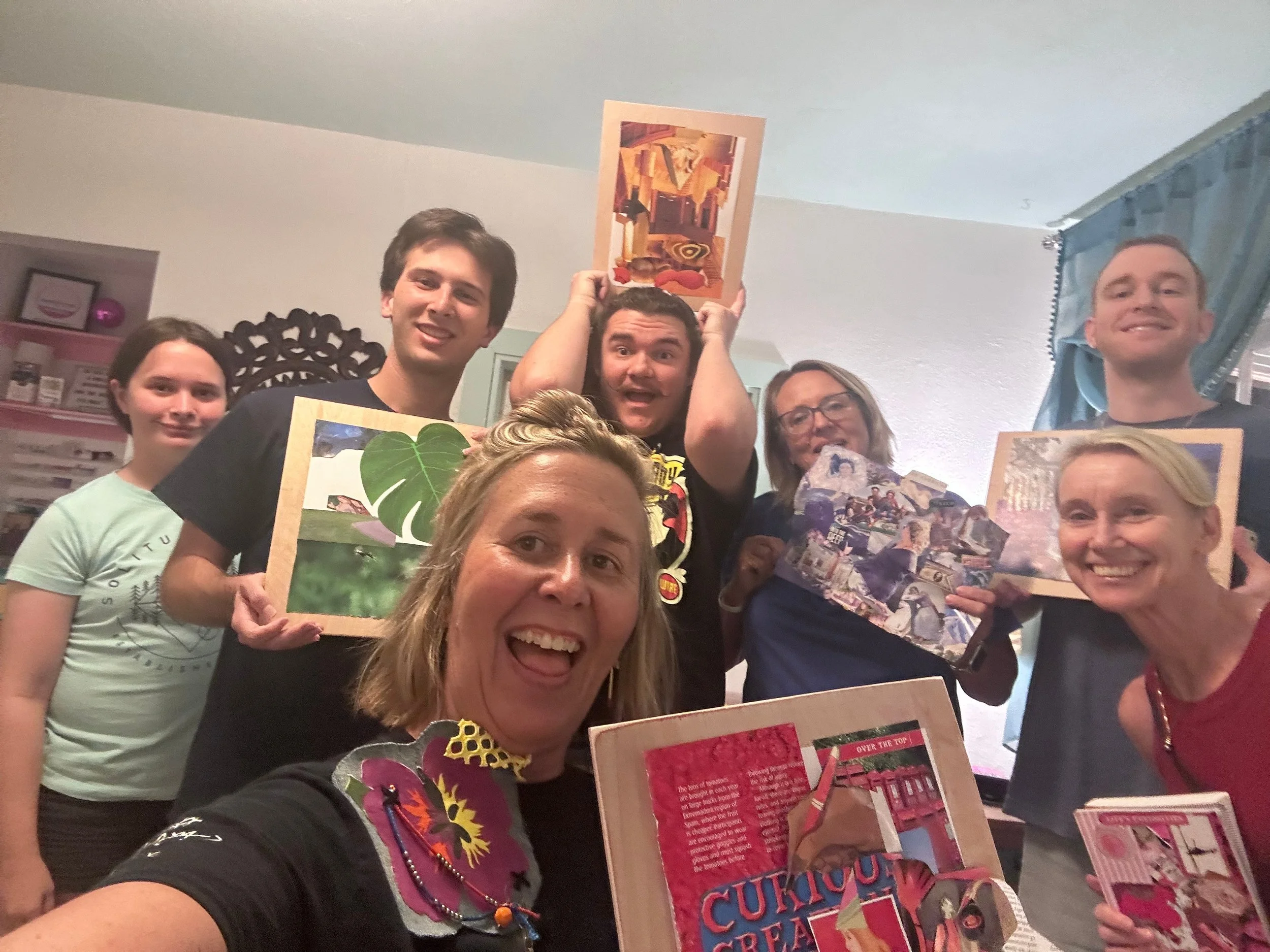 Group of five people gathered indoors, holding colorful magazines and posters, smiling at the camera.