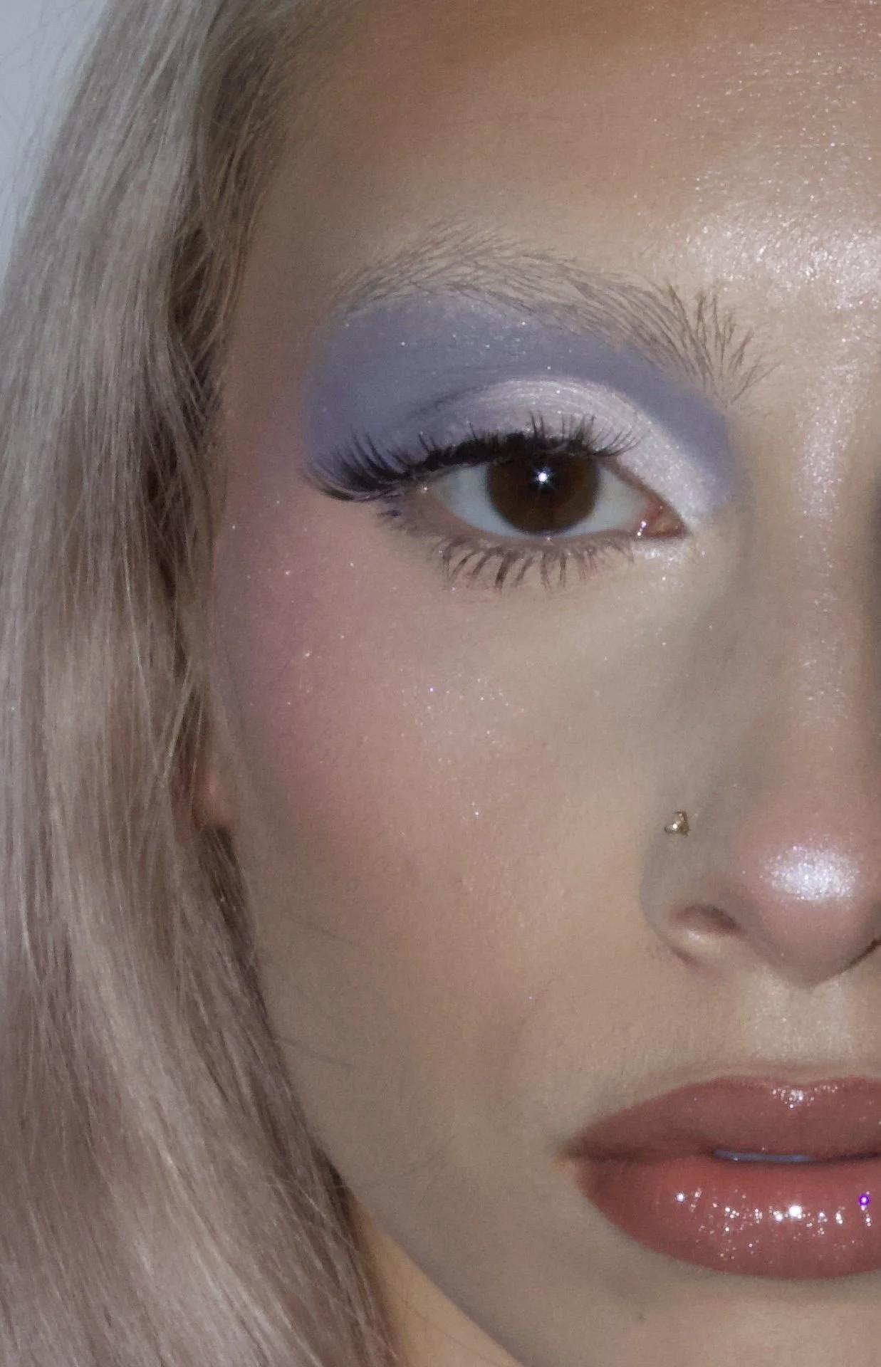 Close-up of a woman's face showing eye makeup with purple lipstick and a nose piercing.