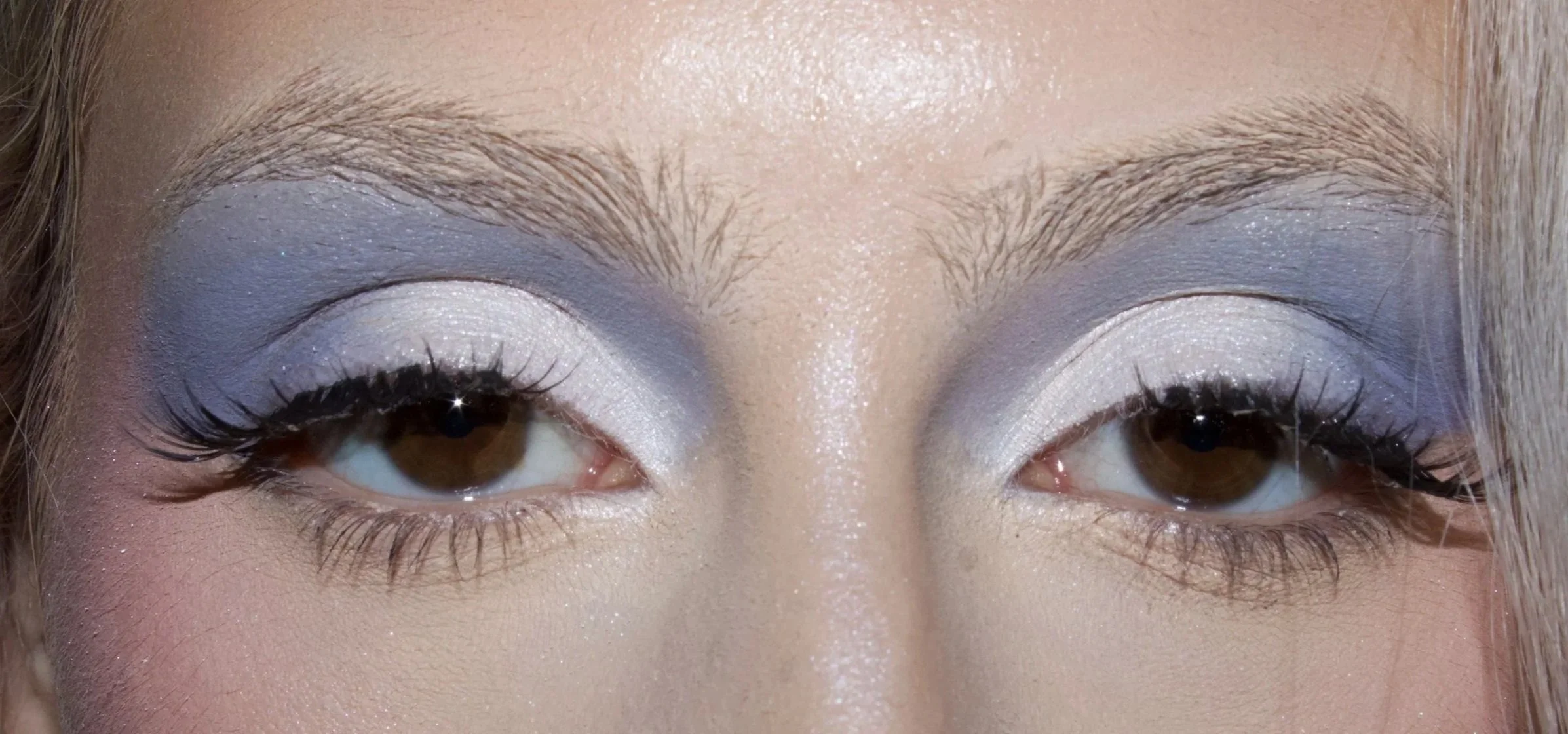 Close-up of a woman's eyes with silver eyeshadow, eyeliner, and mascara, and light-colored eyebrows.