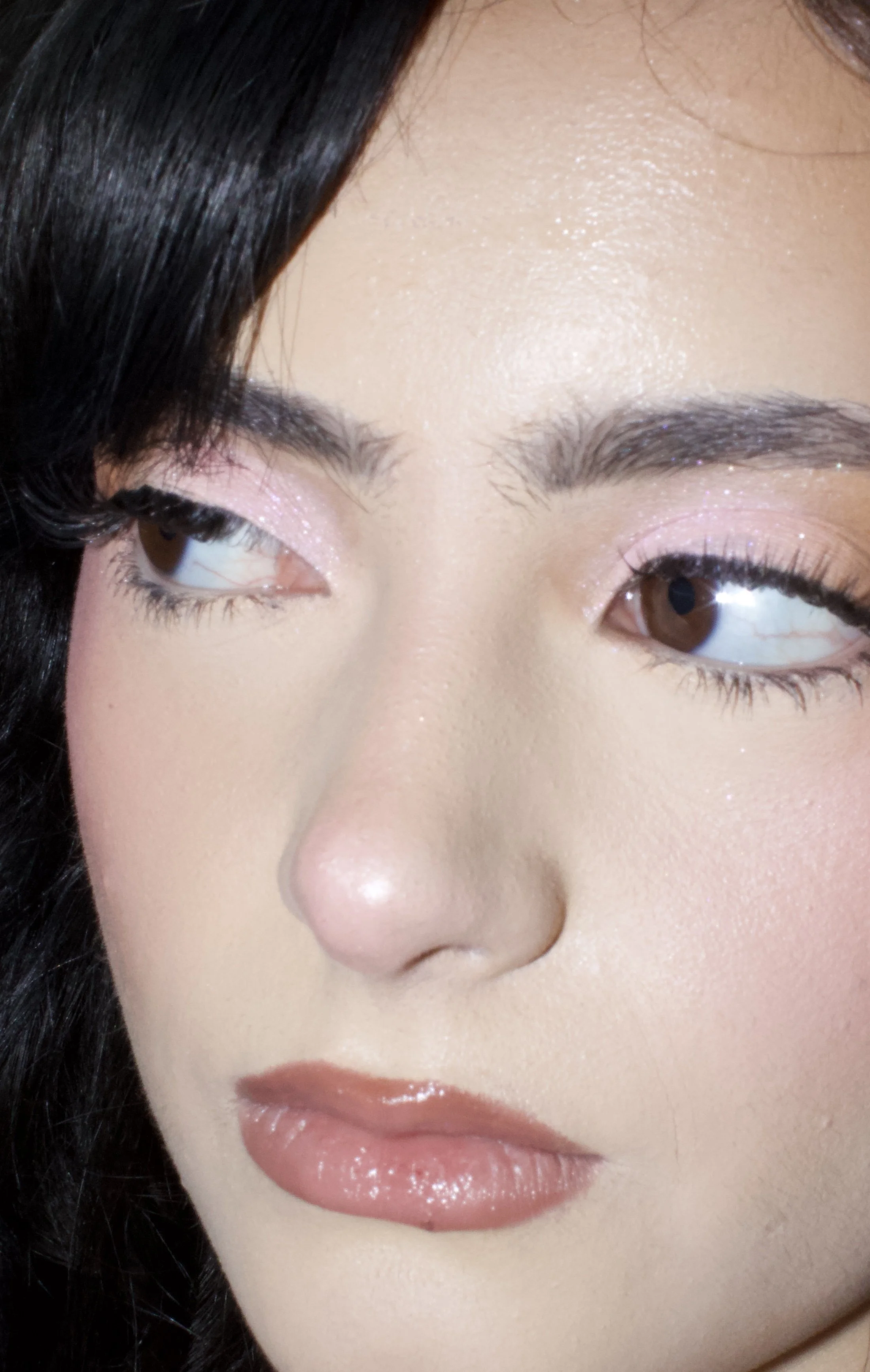 Close-up of a woman's face showing her eyes, nose, and lips with makeup and glossy lips, dark hair, and smooth skin.