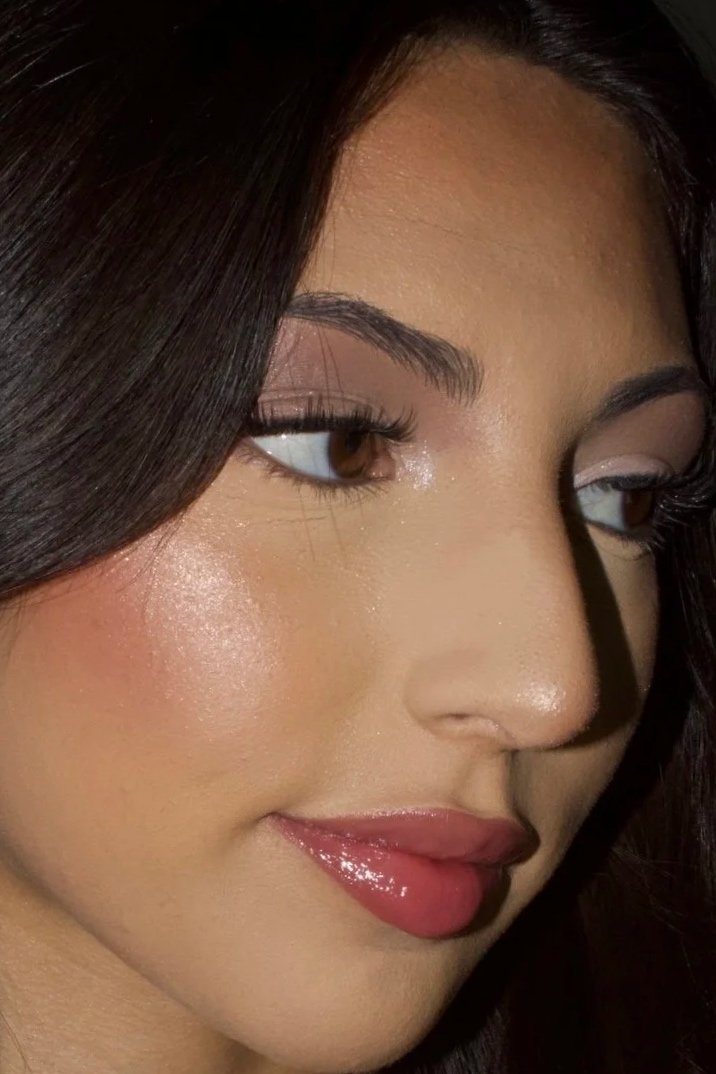 Close-up of a woman's face showing her eye makeup, shiny lips, and smooth skin.