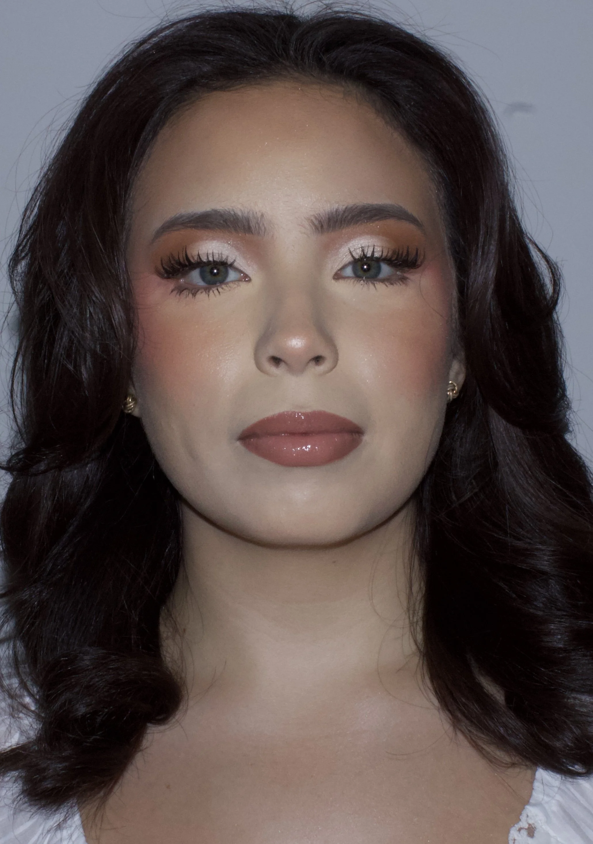 Close-up image of a woman's face, showing makeup with eye shadow, long eyelashes, and lipstick, with dark wavy hair.