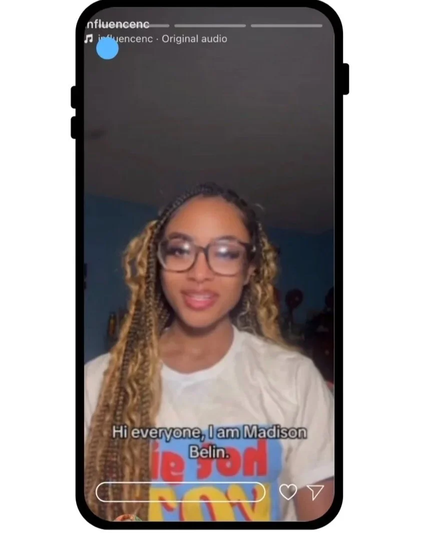 A woman with long, curly blonde hair and glasses introduces herself on a video call, wearing a white T-shirt with colorful text.