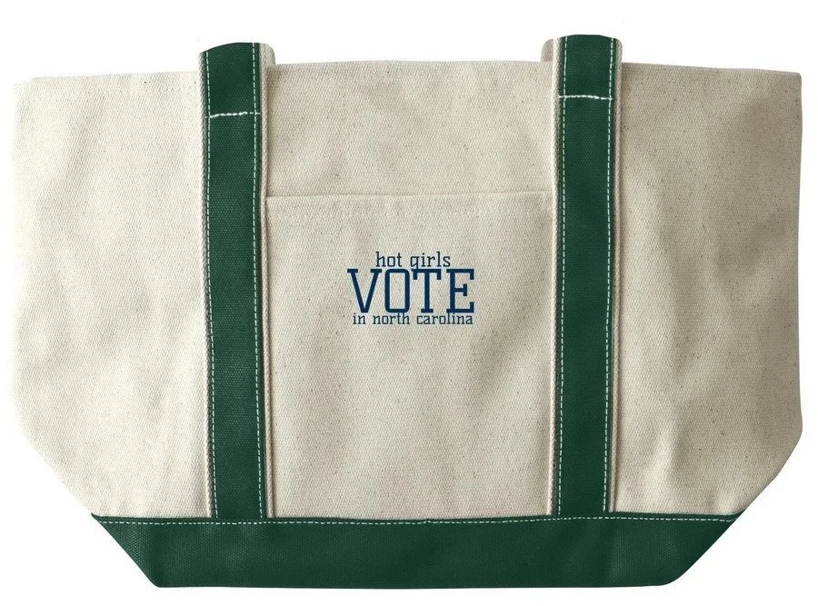 Beige tote bag with green straps and bottom, featuring blue text that reads "hot girls VOTE in north carolina."