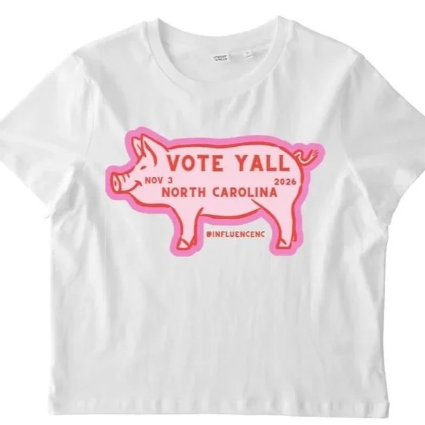 White T-shirt with pink pig-shaped graphic and text promoting voting, referencing North Carolina, with the date November 3, 2026, and the phrase 'Vote Yall'.