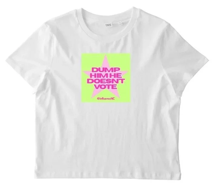 White T-shirt with a pink star and green background, with the text 'DUMP HIM HE DOESN'T VOTE' in pink, and a small handle '@influenceNC' at the bottom.