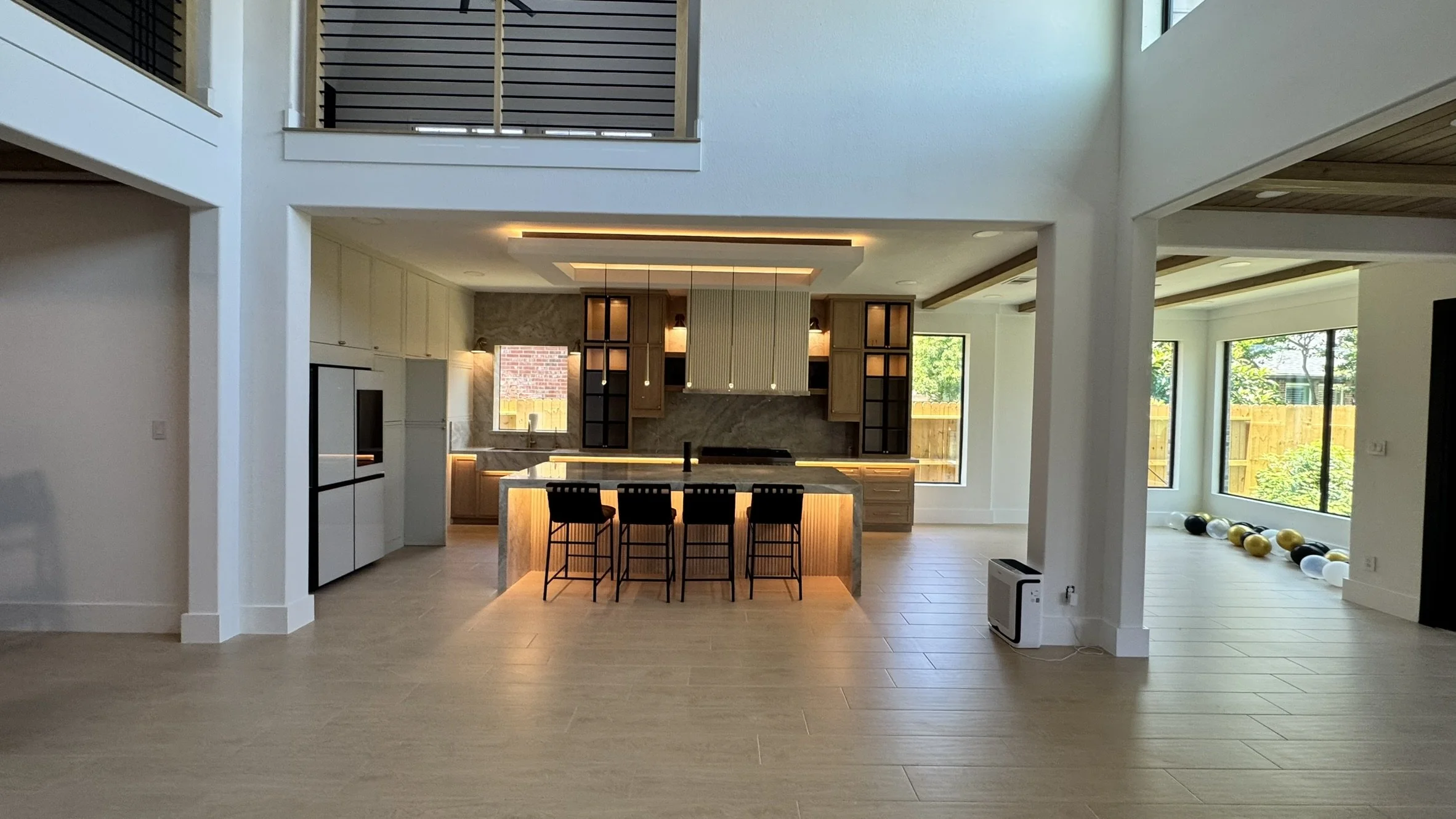 Open-concept modern kitchen and living area with large windows, wooden accents, and a row of black and gold exercise balls on the floor.