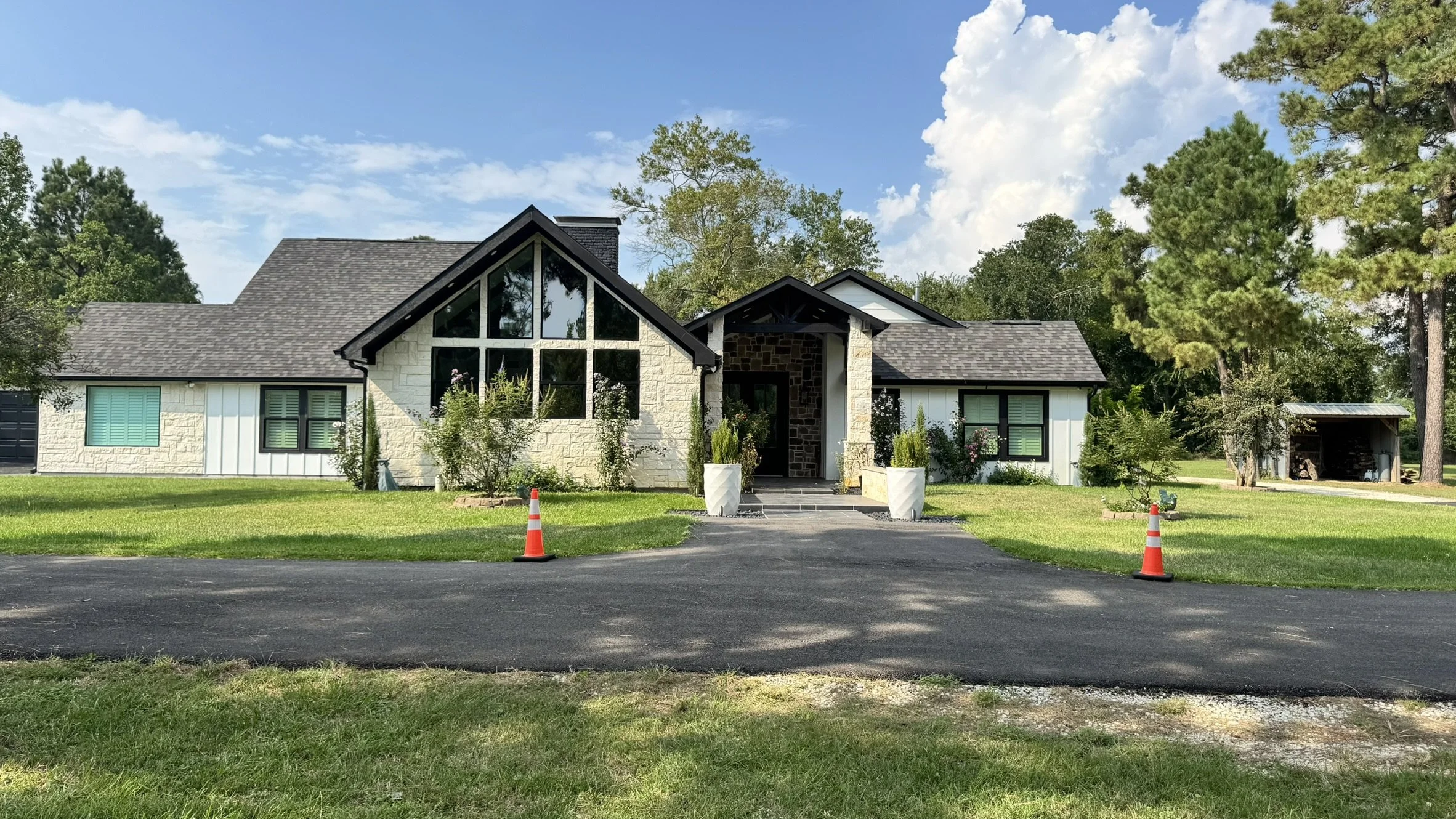 Front view of a modern house with a gabled roof, large windows, and a landscaped front yard with two orange traffic cones on the driveway.