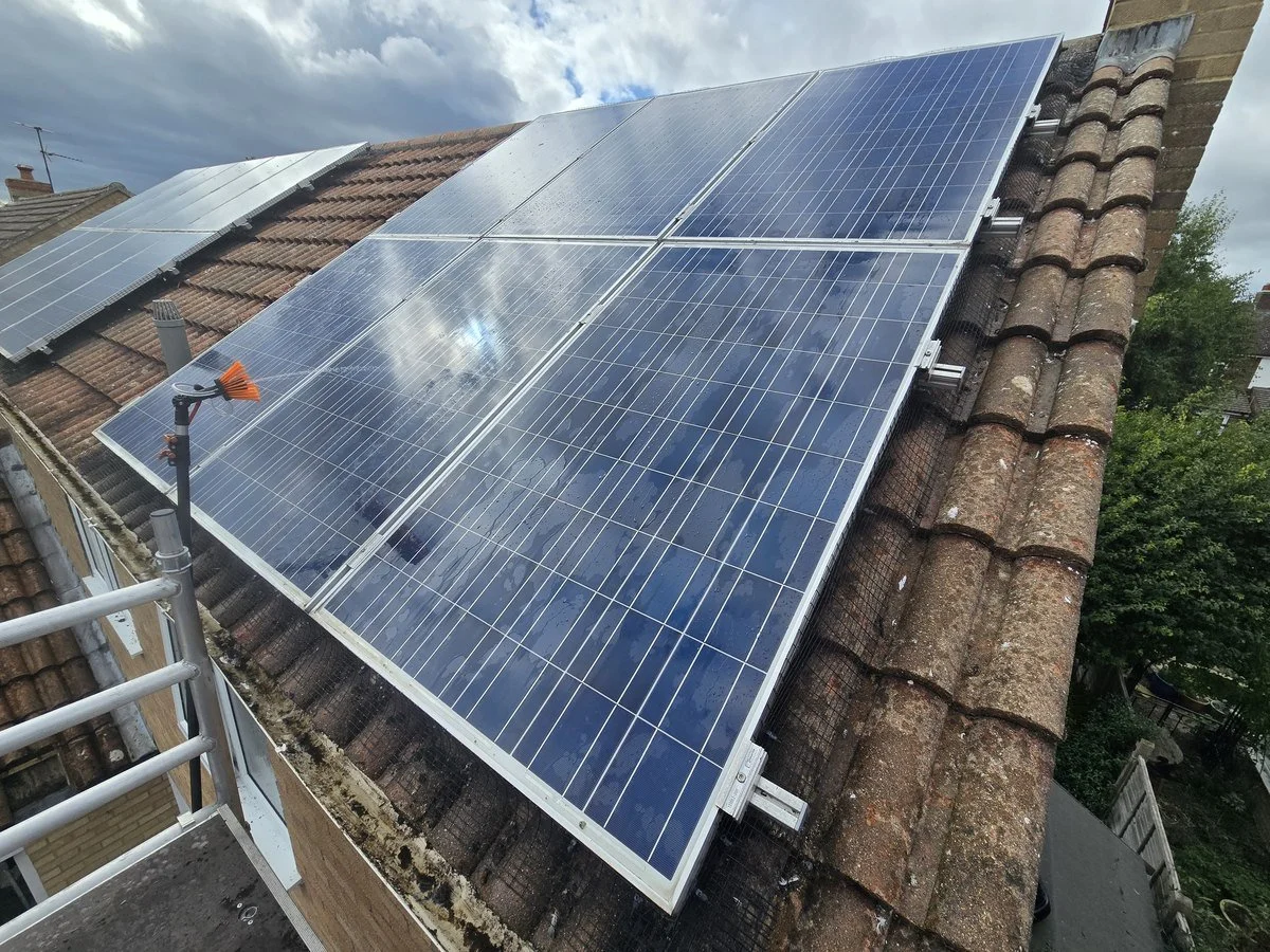 Solar panels installed on a tiled roof of a house, with a cloudy sky in the background.