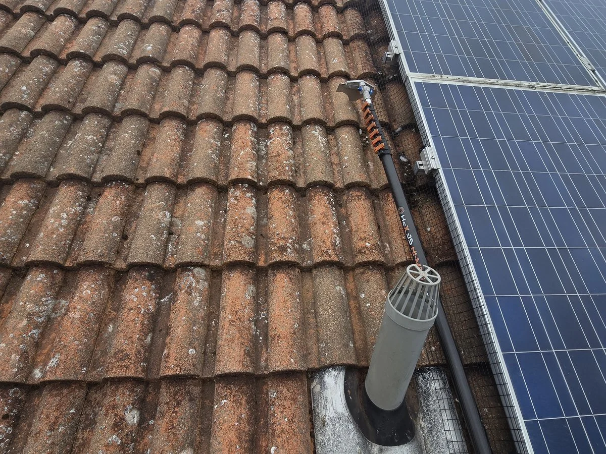 Rooftop with weathered clay tiles, solar panels, a vent pipe, and a roof-mounted antenna.