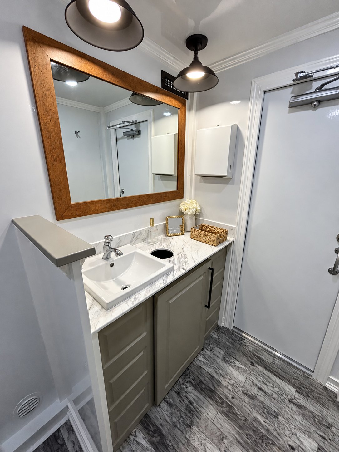 Interior of Southern Squat luxury restroom trailer featuring an elegant vanity, framed mirror, modern lighting, and wood-look flooring for weddings and events in South Carolina.