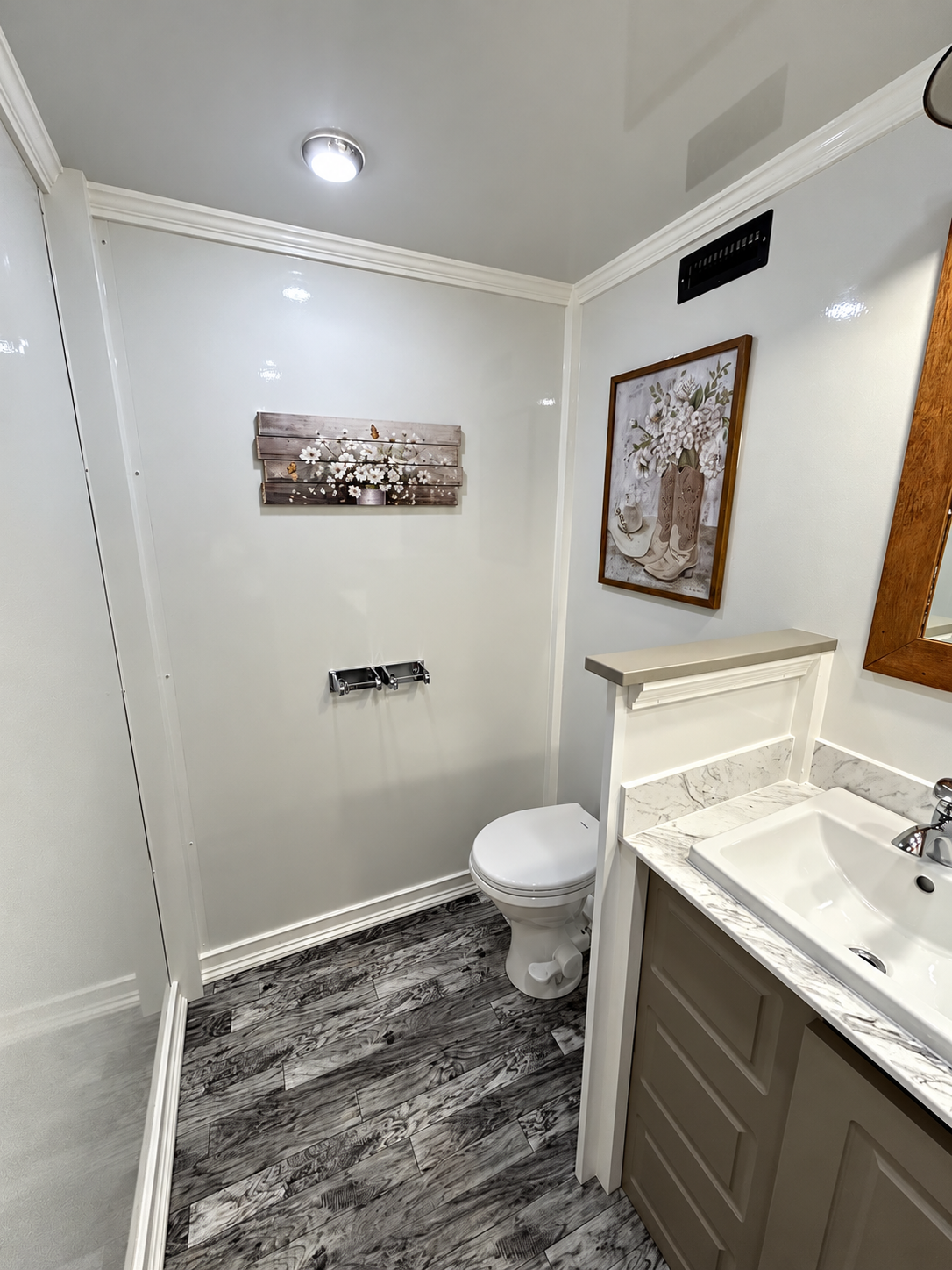 A small bathroom with white walls, dark wood flooring, a toilet, a vanity with a sink, and decorative artwork on the walls.