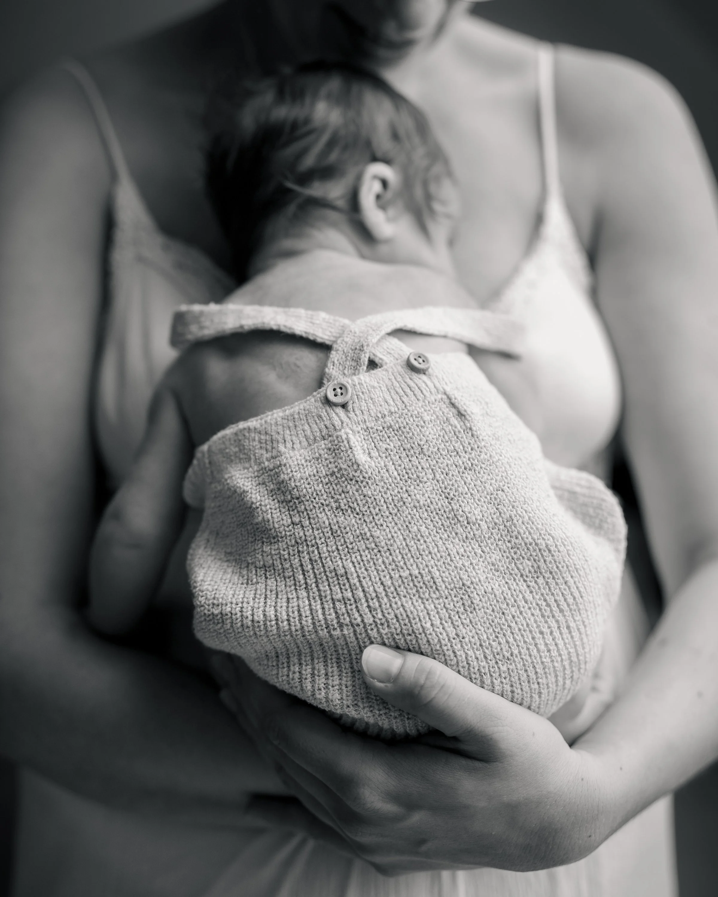 Ein Baby wird auf der Brust einer Frau gestillt, beide tragen Nachthemden. Die Szene ist in Schwarzweiß gehalten.