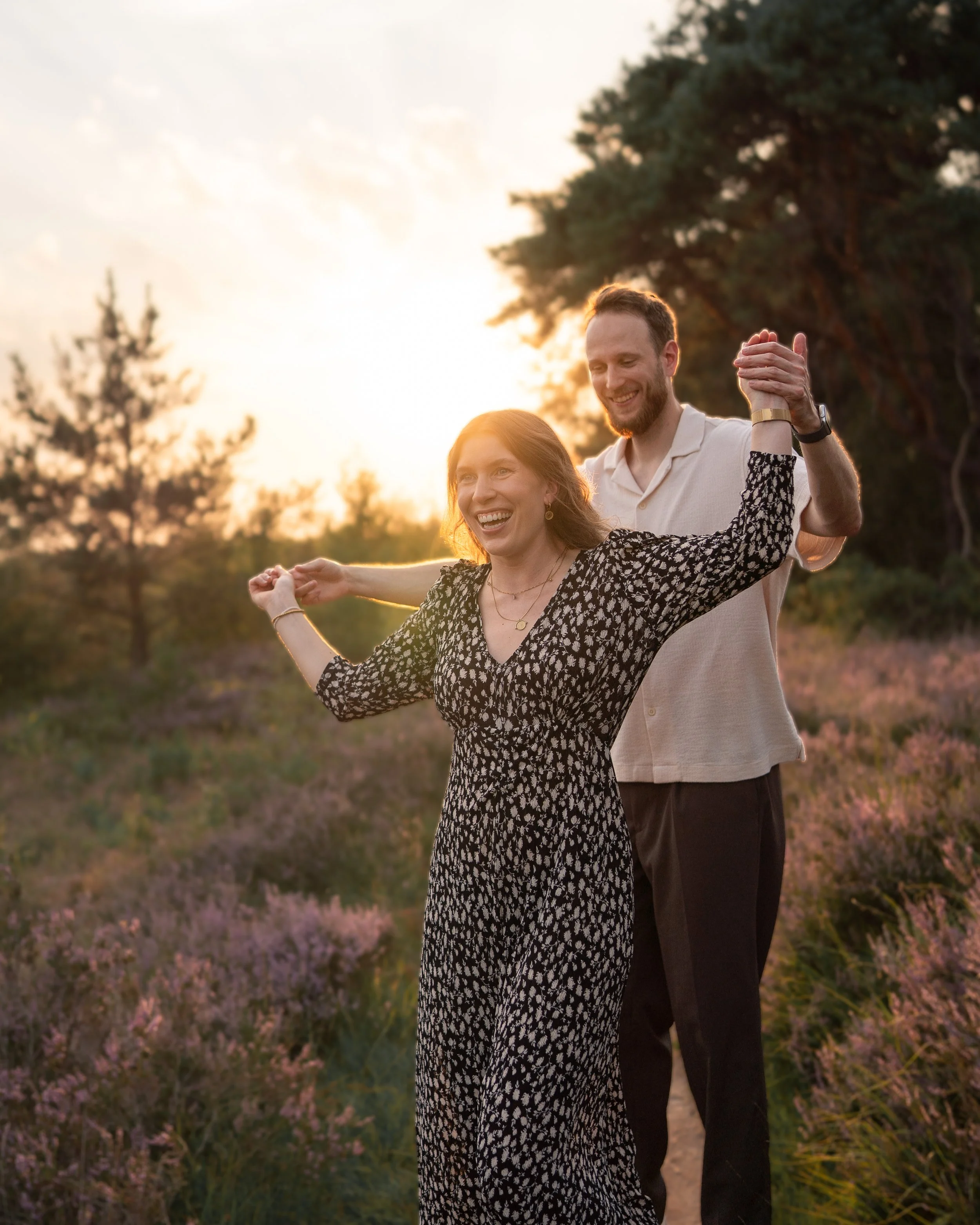 Ein Paar tanzt Hand in Hand im Freien bei Sonnenuntergang, umgeben von Natur mit Bäumen und Blüten