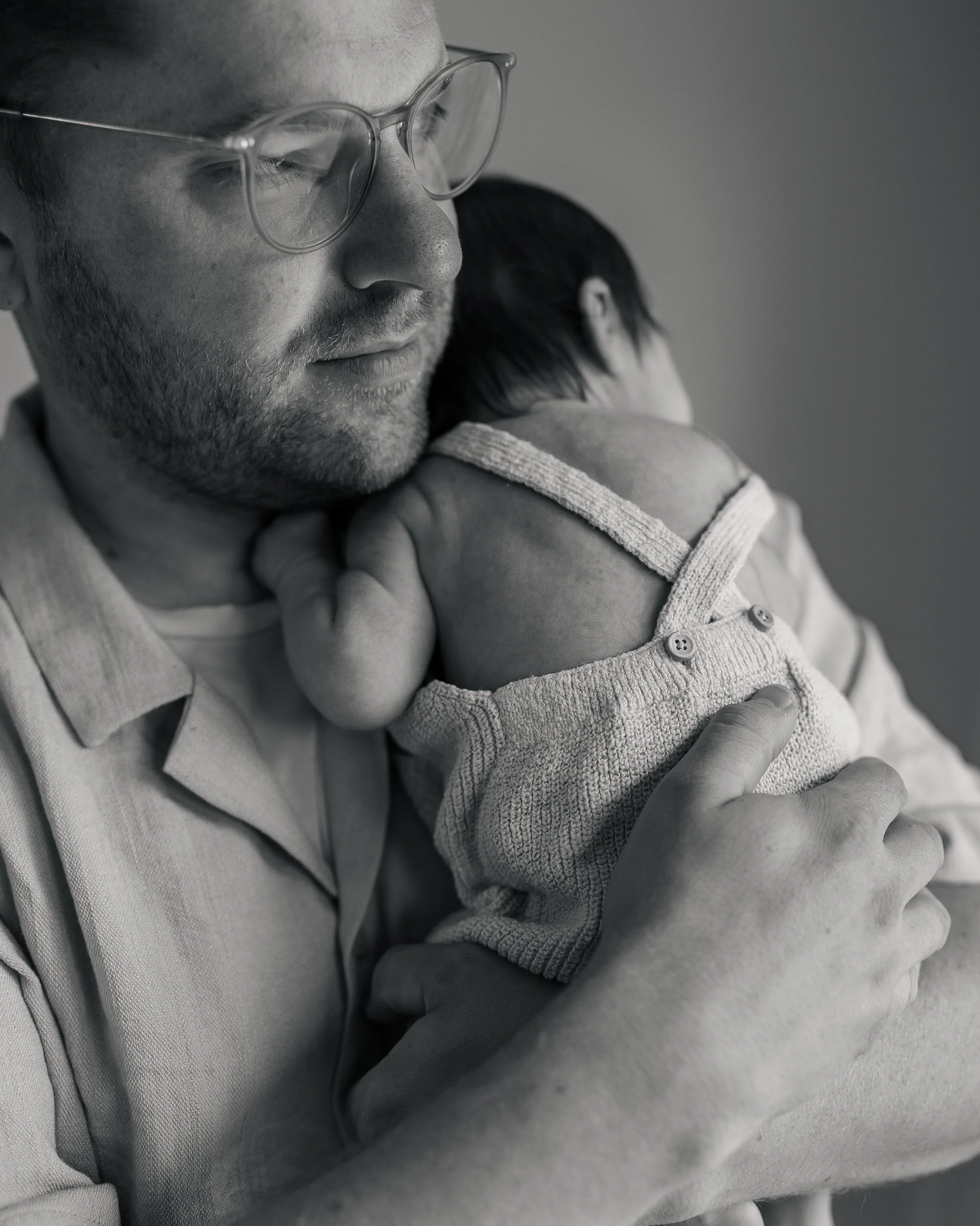 Ein Mann mit Brille hält ein Kind im Arm, beide in einem emotionalen Moment, schwarz-weiß Fotografie.