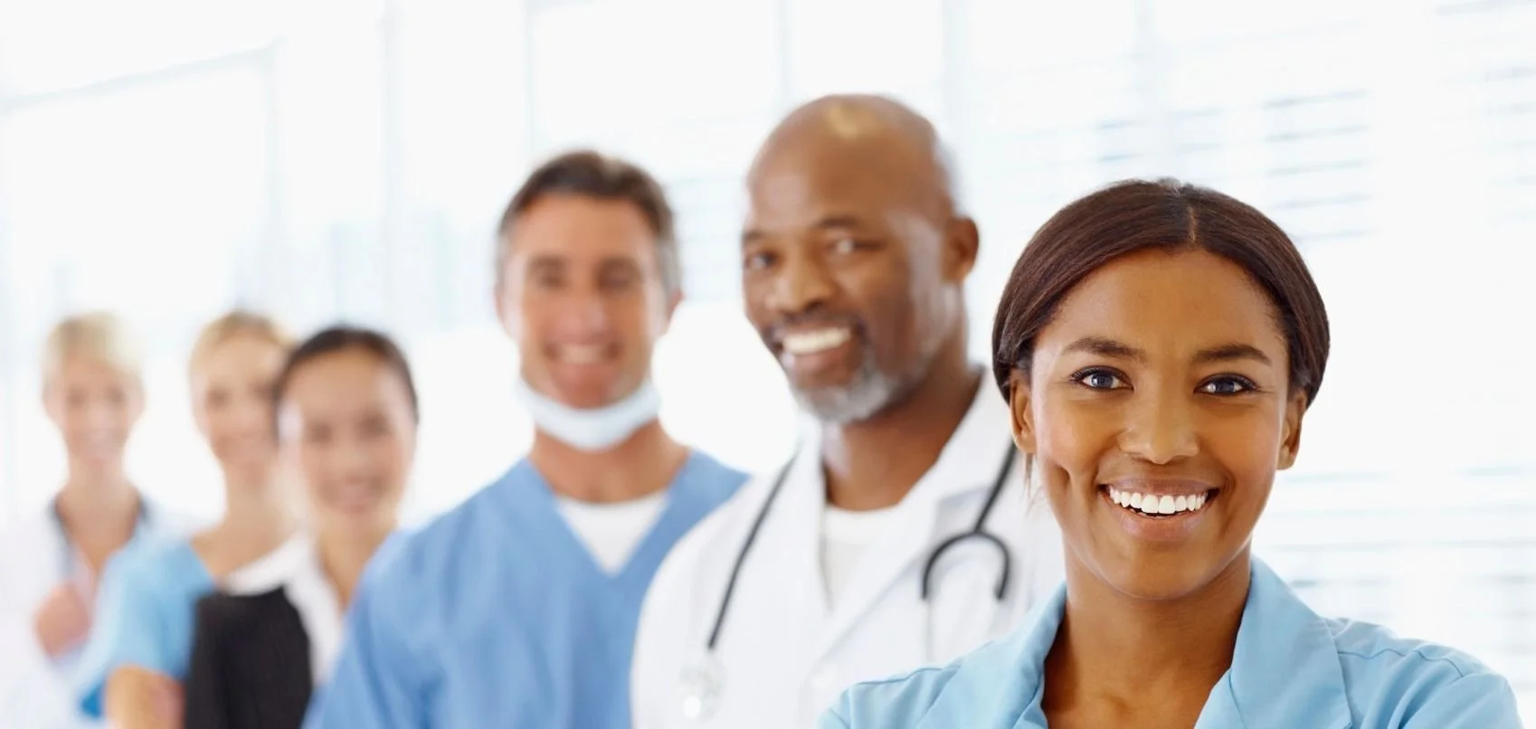 A diverse group of healthcare professionals, including doctors and nurses, smiling in a hospital or clinic setting.