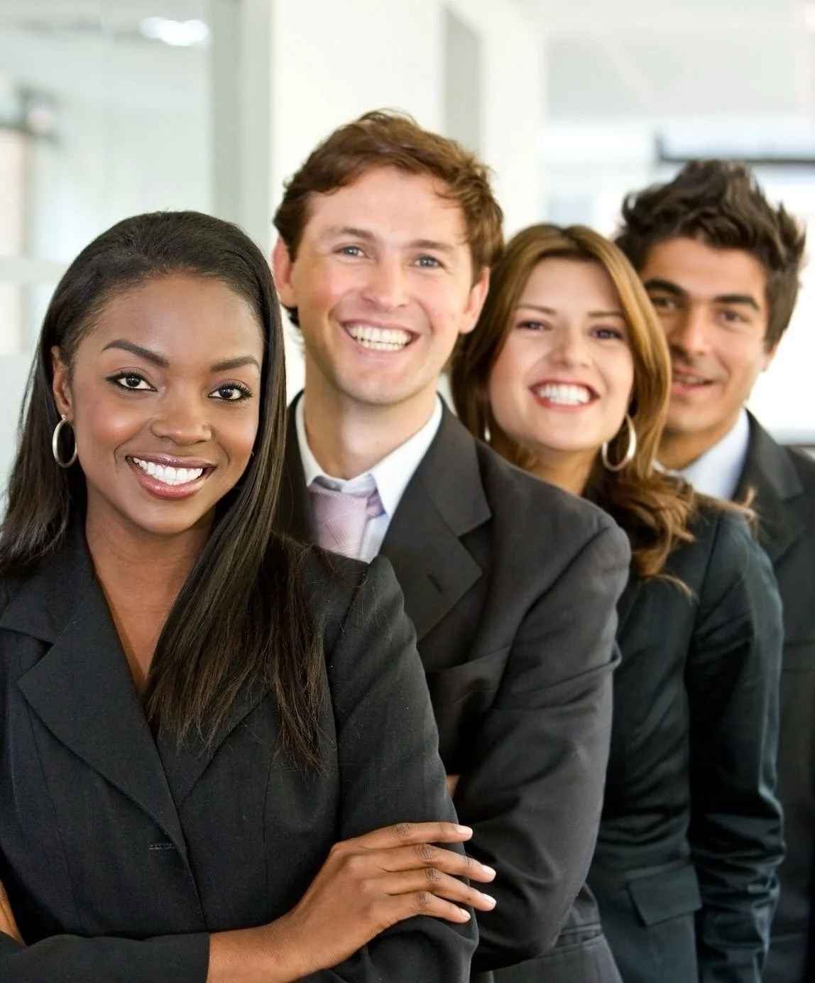 Four diverse professionals dressed in business suits smiling and standing in a line in an office setting.