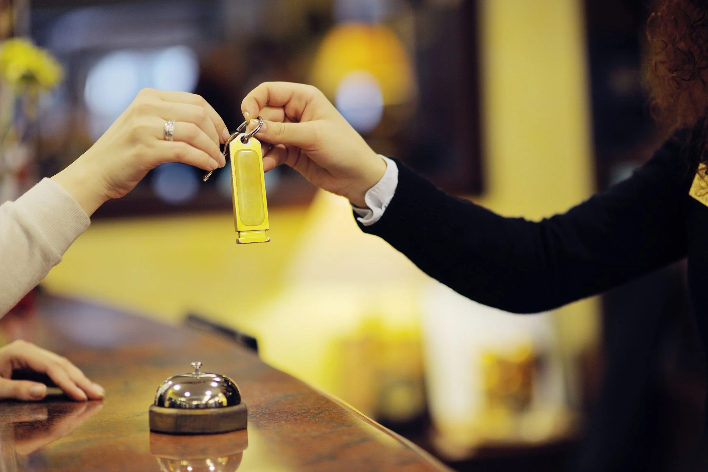 A person is pressing a service bell on a counter while another person holds a yellow keychain, potentially to summon assistance.