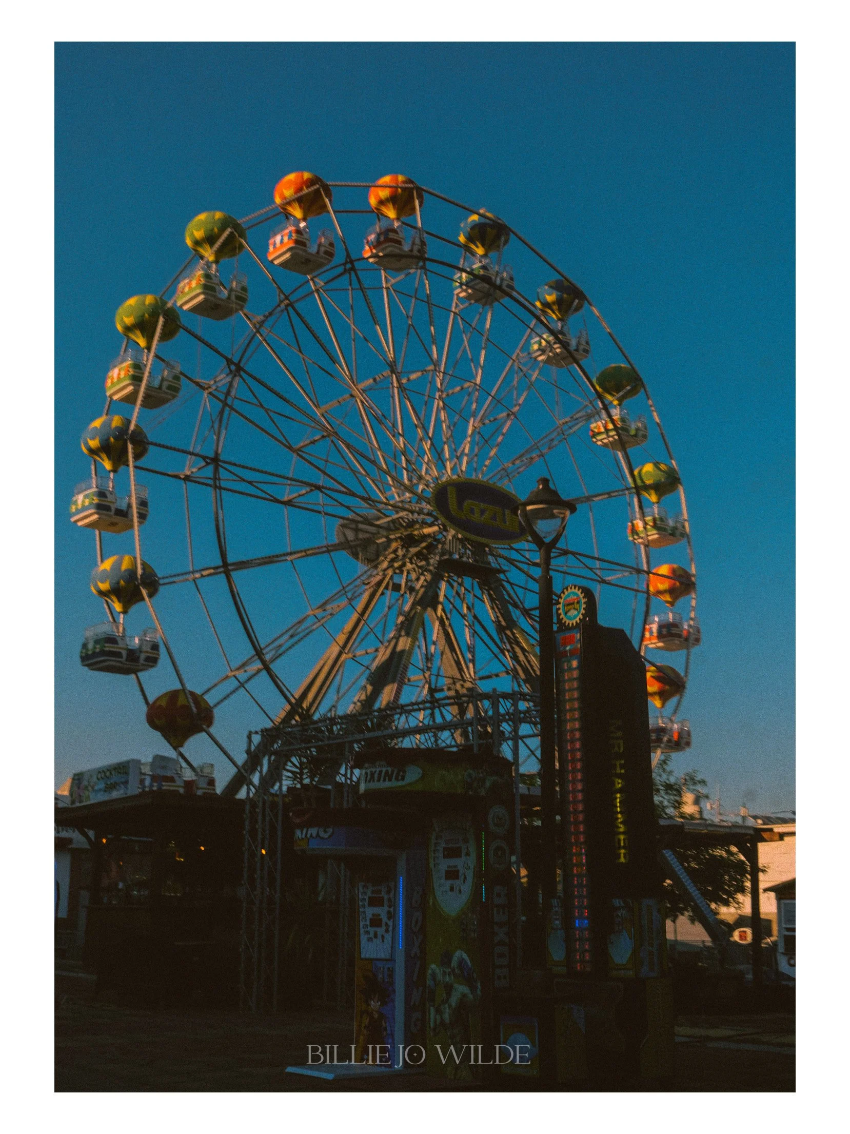 Photo of a Ferris wheel at a carnival during dusk, with a sign reading 'Billie Jo Wilde' at the bottom.