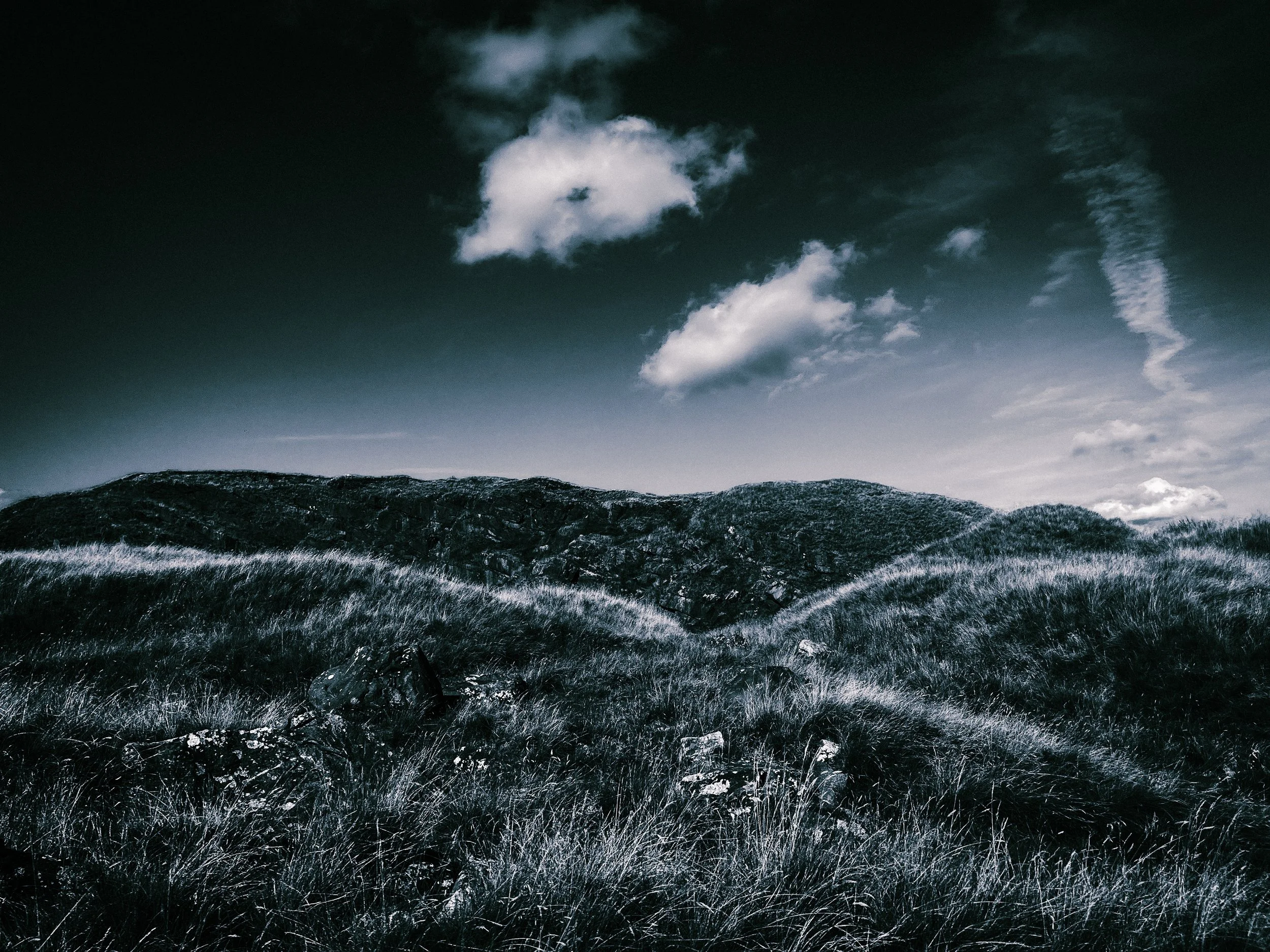 A landscape scene with rolling hills or mountains under a cloudy sky, in a monochrome or desaturated color scheme.