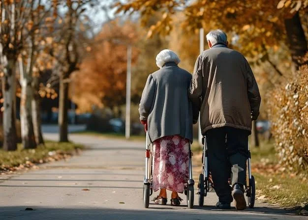 An elderly couple walking together with walkers on a leaf-covered sidewalk in autumn.