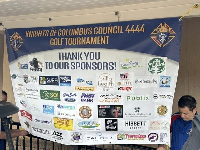 A large banner for the Knights of Columbus Council 4444 Golf Tournament displays sponsor logos and a thank you message.