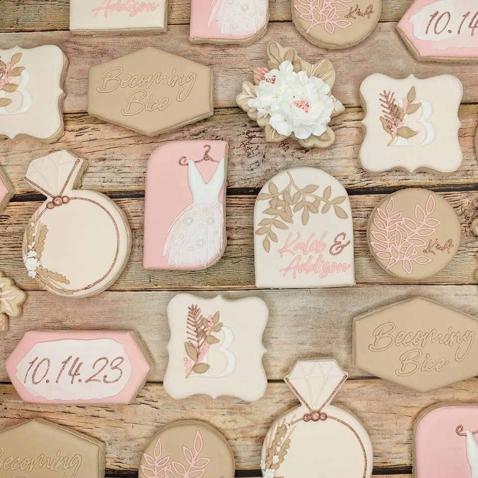 Boho decorative cookies with wedding and bridal themes, featuring floral patterns, bridal dress, date, and names, arranged on a wooden surface.
