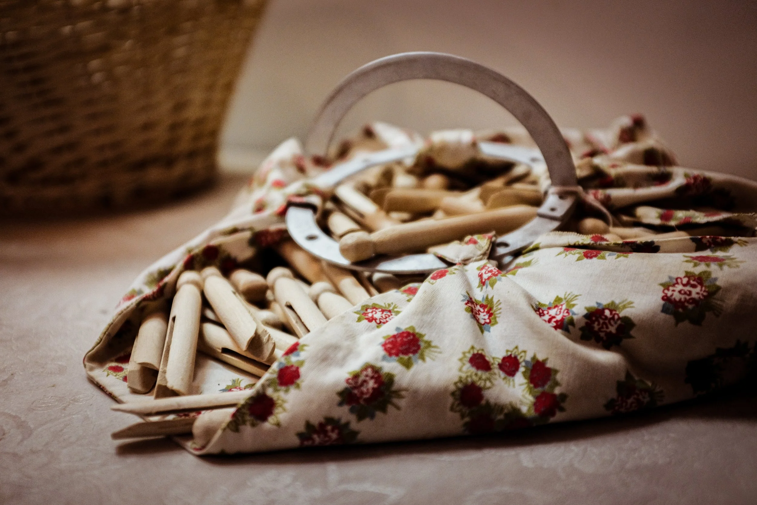A pile of wooden clothespins placed on a floral fabric cloth, with a wicker basket partially visible in the background.