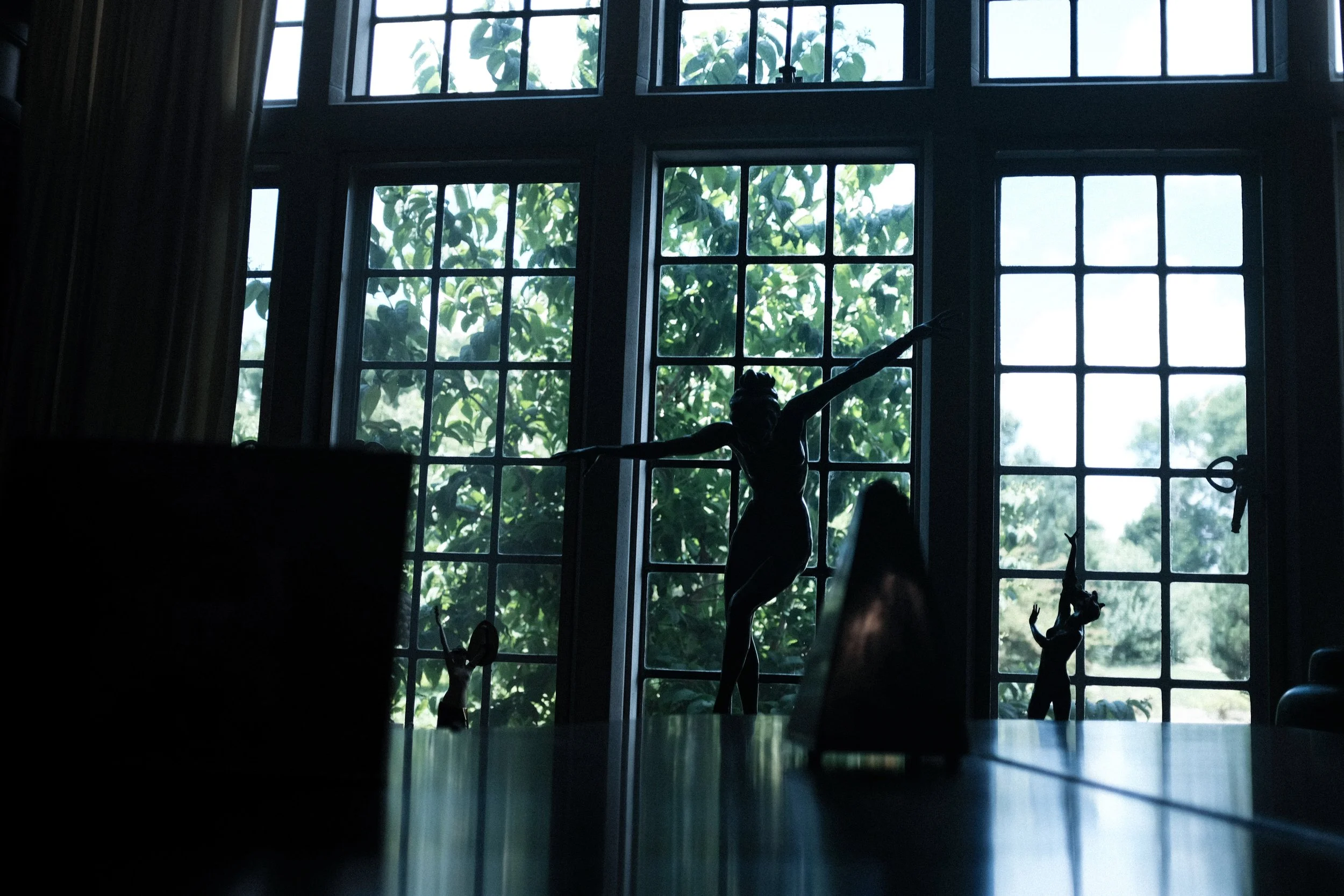 Silhouettes of small toy figures on a table in front of large window with green trees outside.