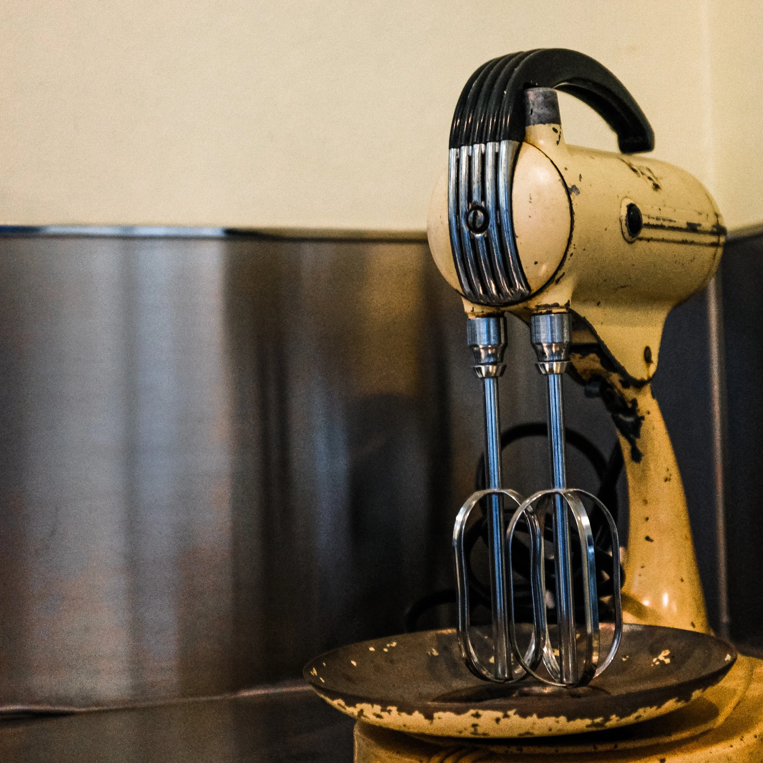 Close-up of a vintage beige and black electric tool or machine with metal components, set against a plain background.