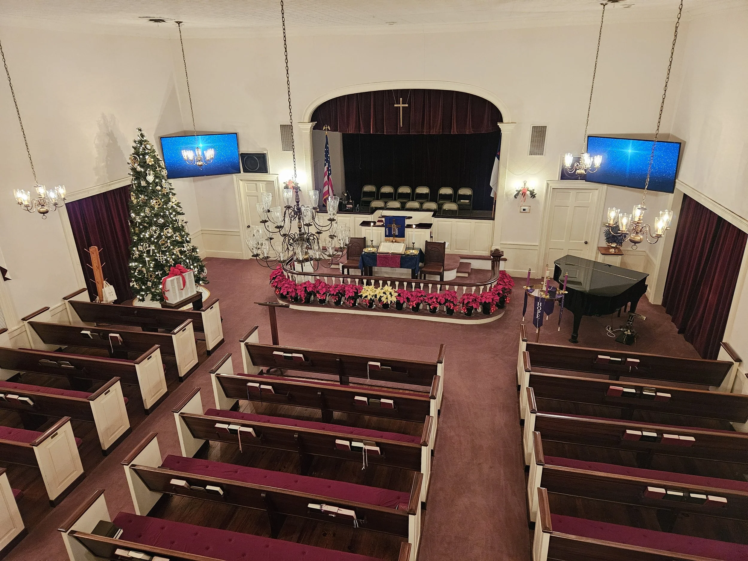 Interior of a church with a Christmas tree, poinsettias, a pulpit with a cross, and seating area for congregation.